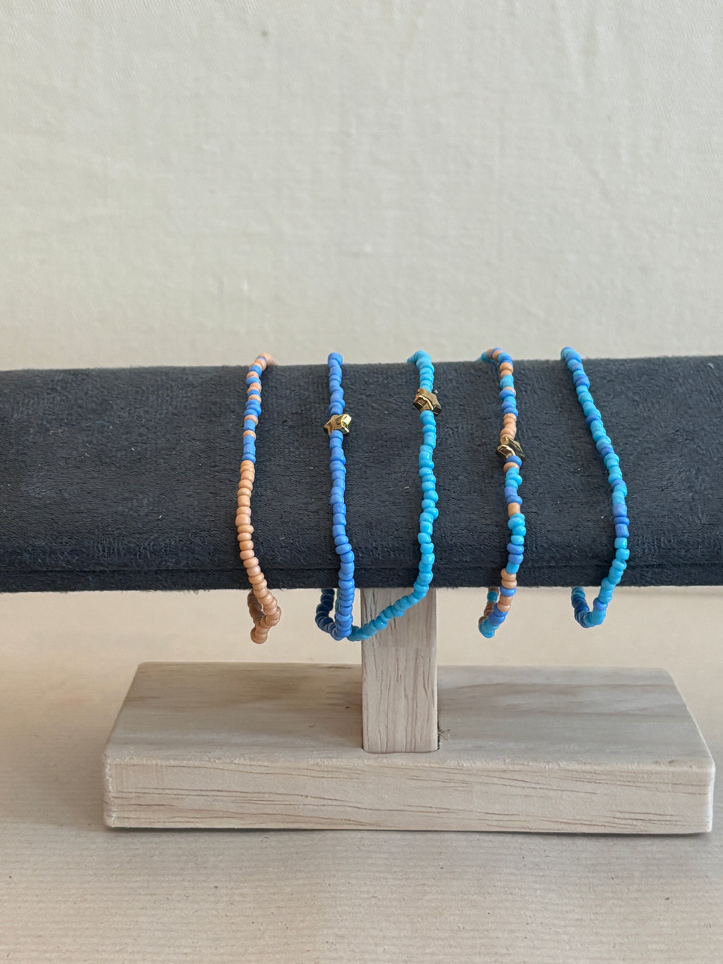 Blue beaded bracelets on a dark fabric background with a wooden block.