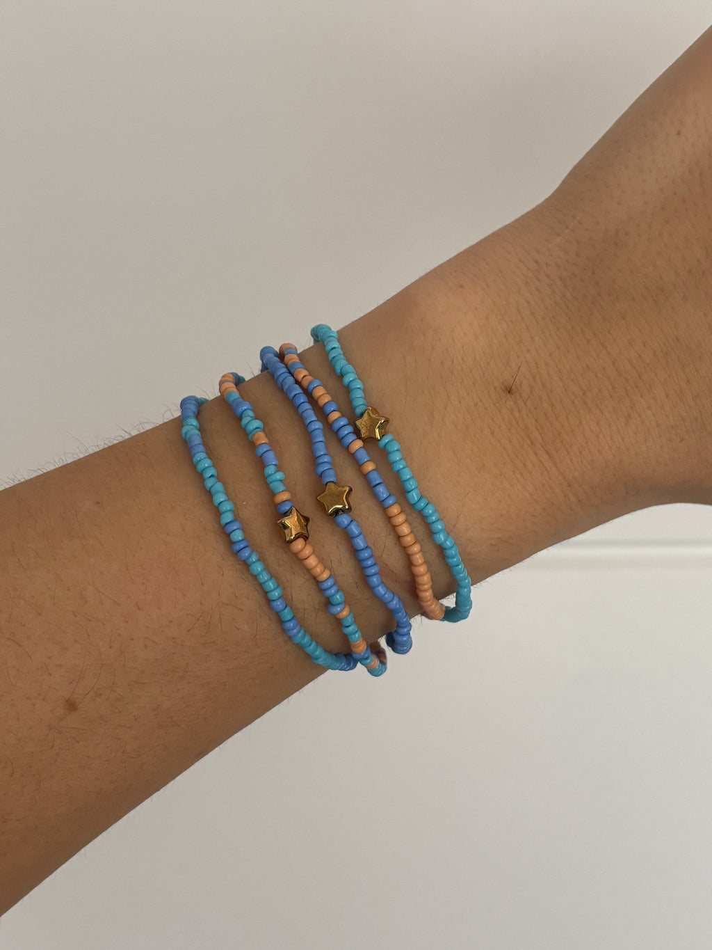 Wrist wearing multiple blue and orange beaded bracelets on a plain background