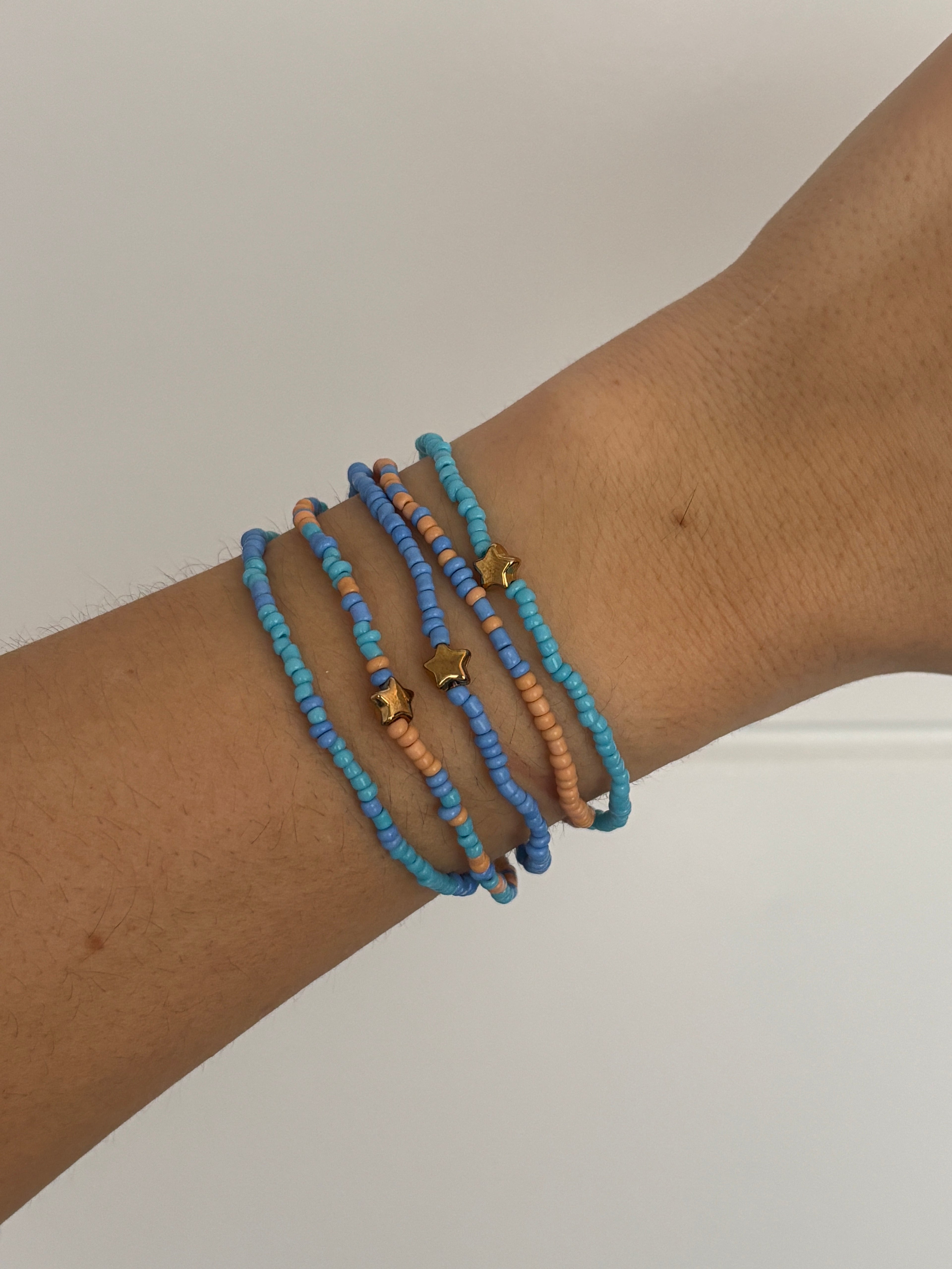 Wrist wearing multiple blue and orange beaded bracelets on a plain background