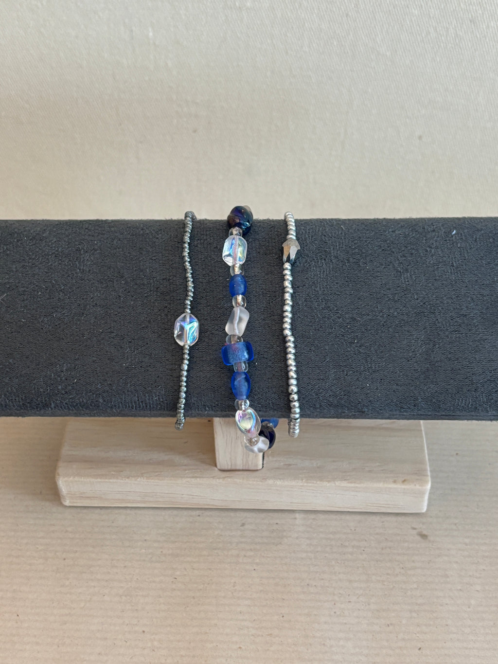 Three beaded bracelets on a gray stand against a beige background
