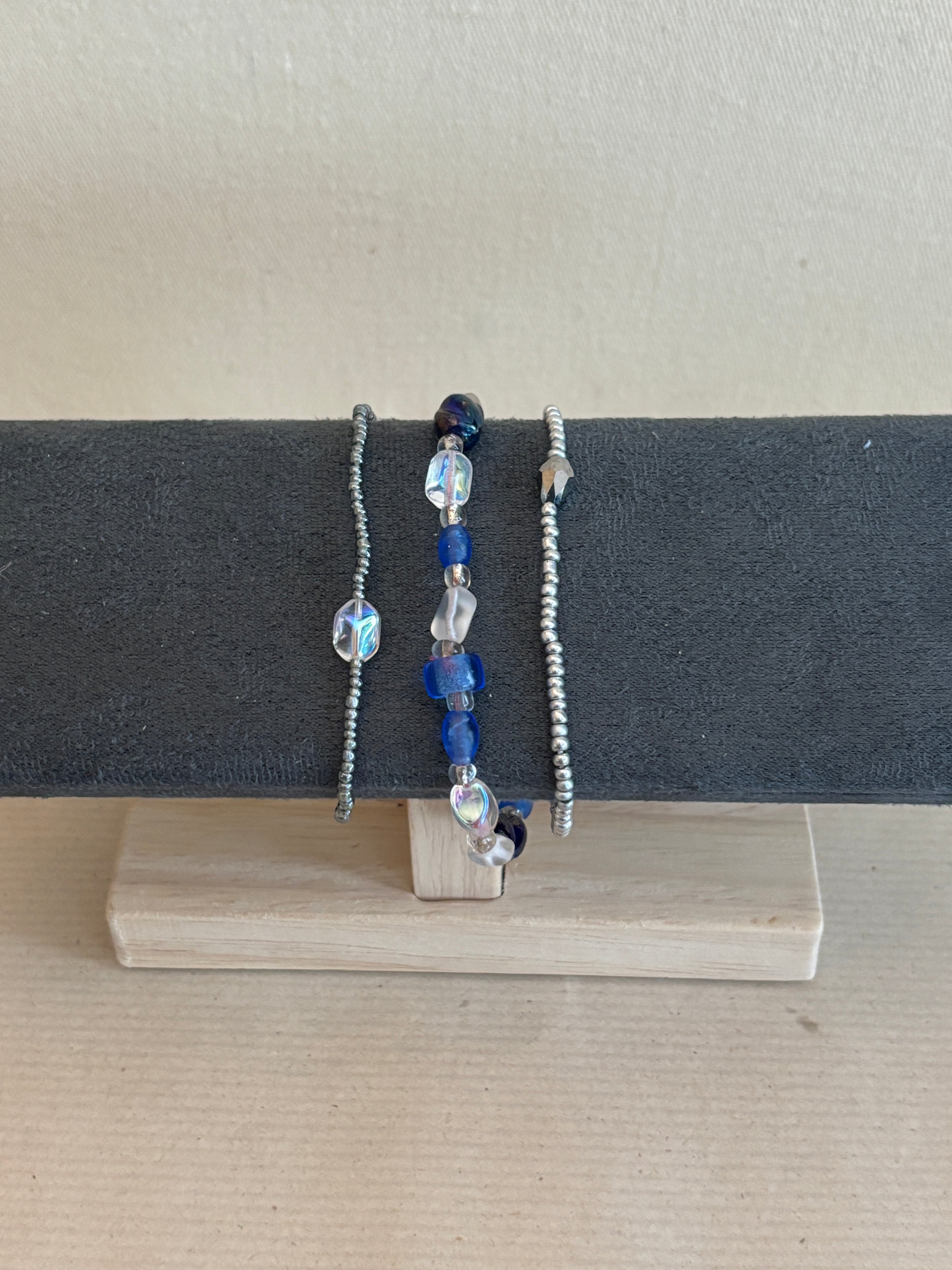 Three beaded bracelets on a gray stand against a beige background