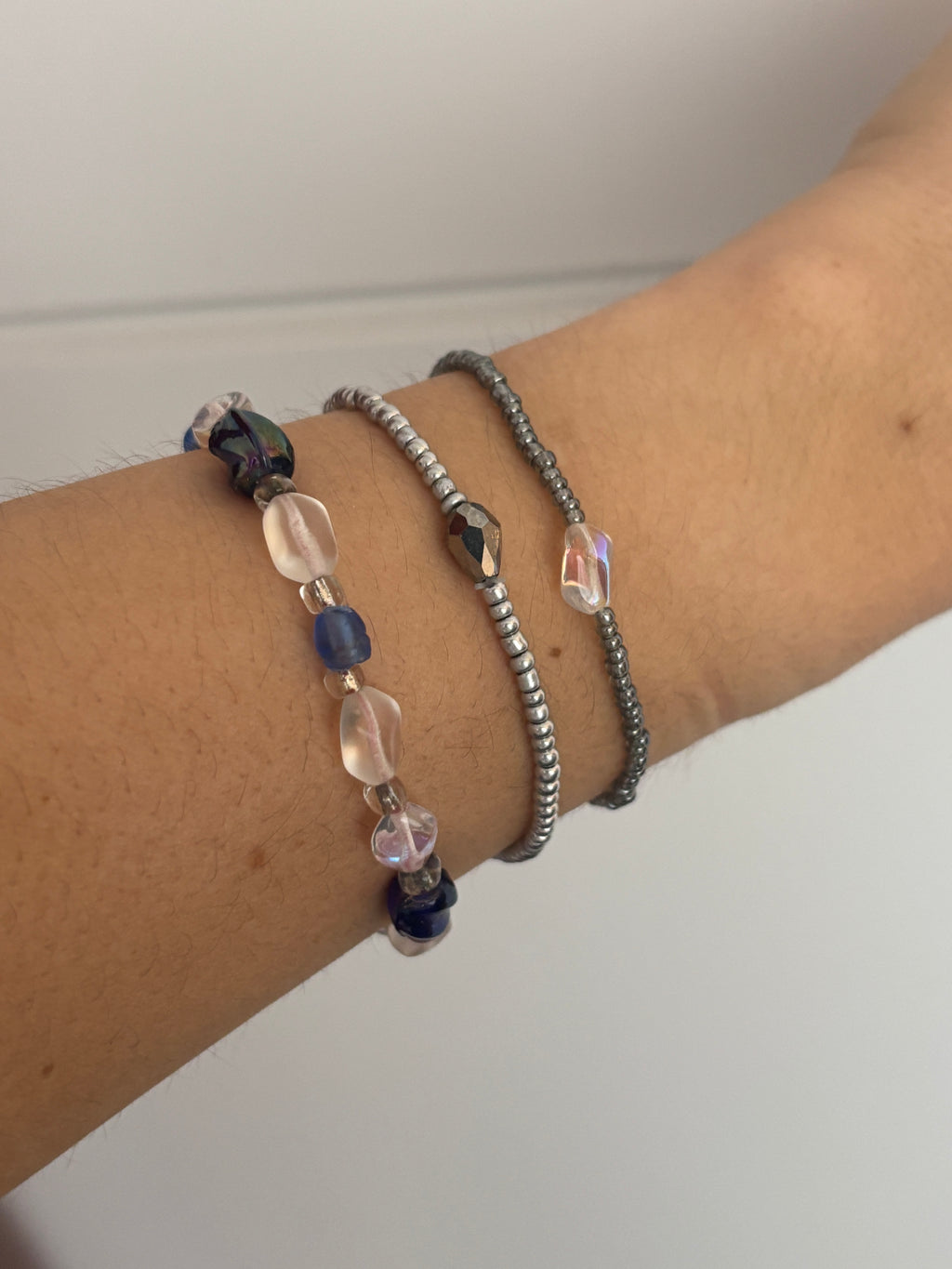 Close-up of a wrist wearing multiple beaded bracelets on a plain background