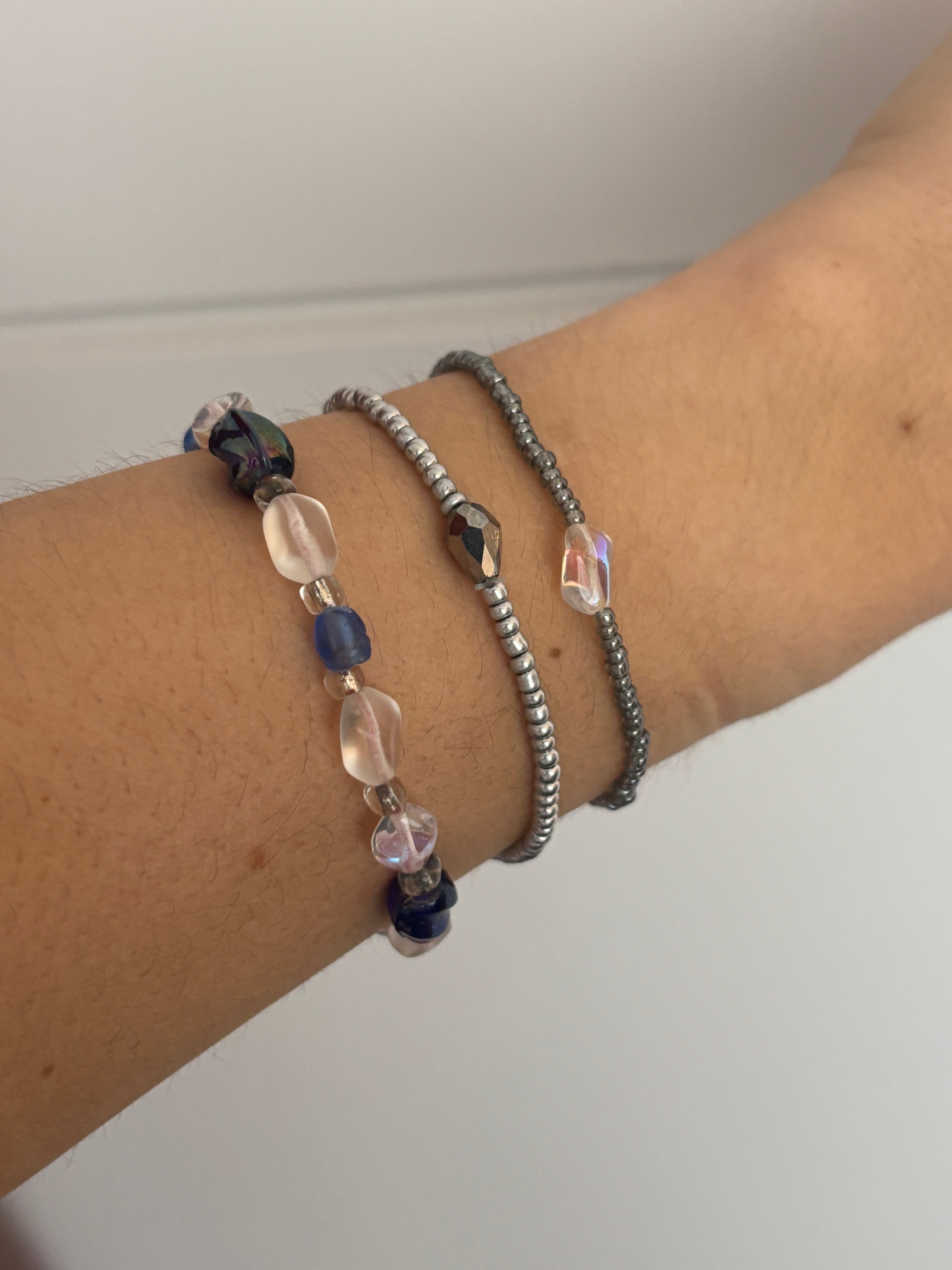 Close-up of a wrist wearing multiple beaded bracelets on a plain background