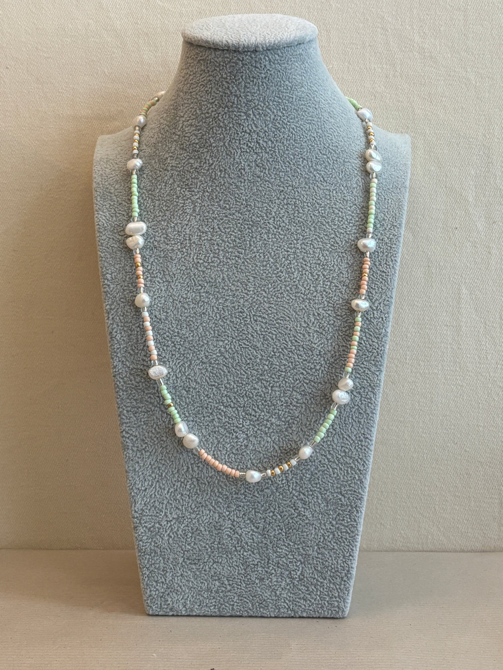 Pearl necklace on a gray jewelry display block against a beige background