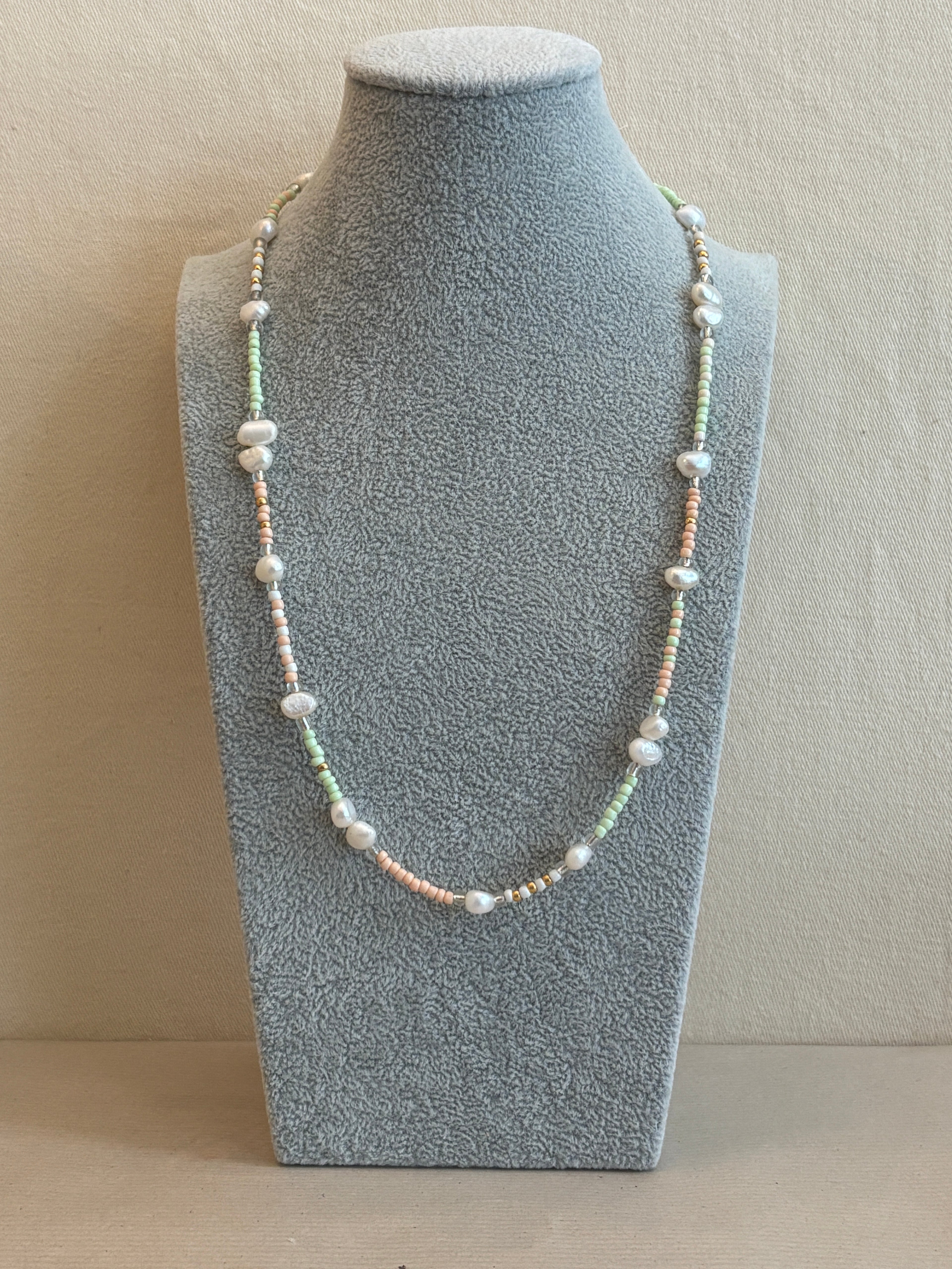 Pearl necklace on a gray jewelry display block against a beige background
