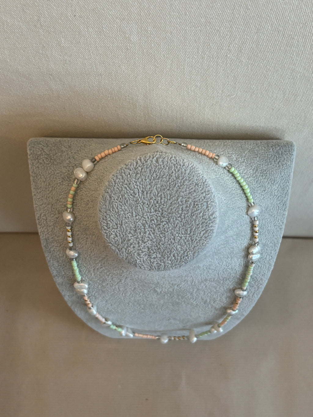 Beaded necklace on a gray stand against a beige background