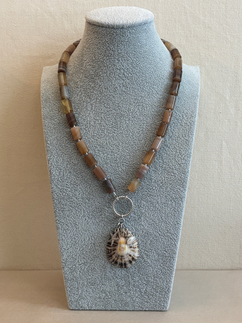 Necklace with a shell pendant on a gray stand against a beige background