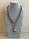 Necklace with a shell pendant on a gray stand against a beige background