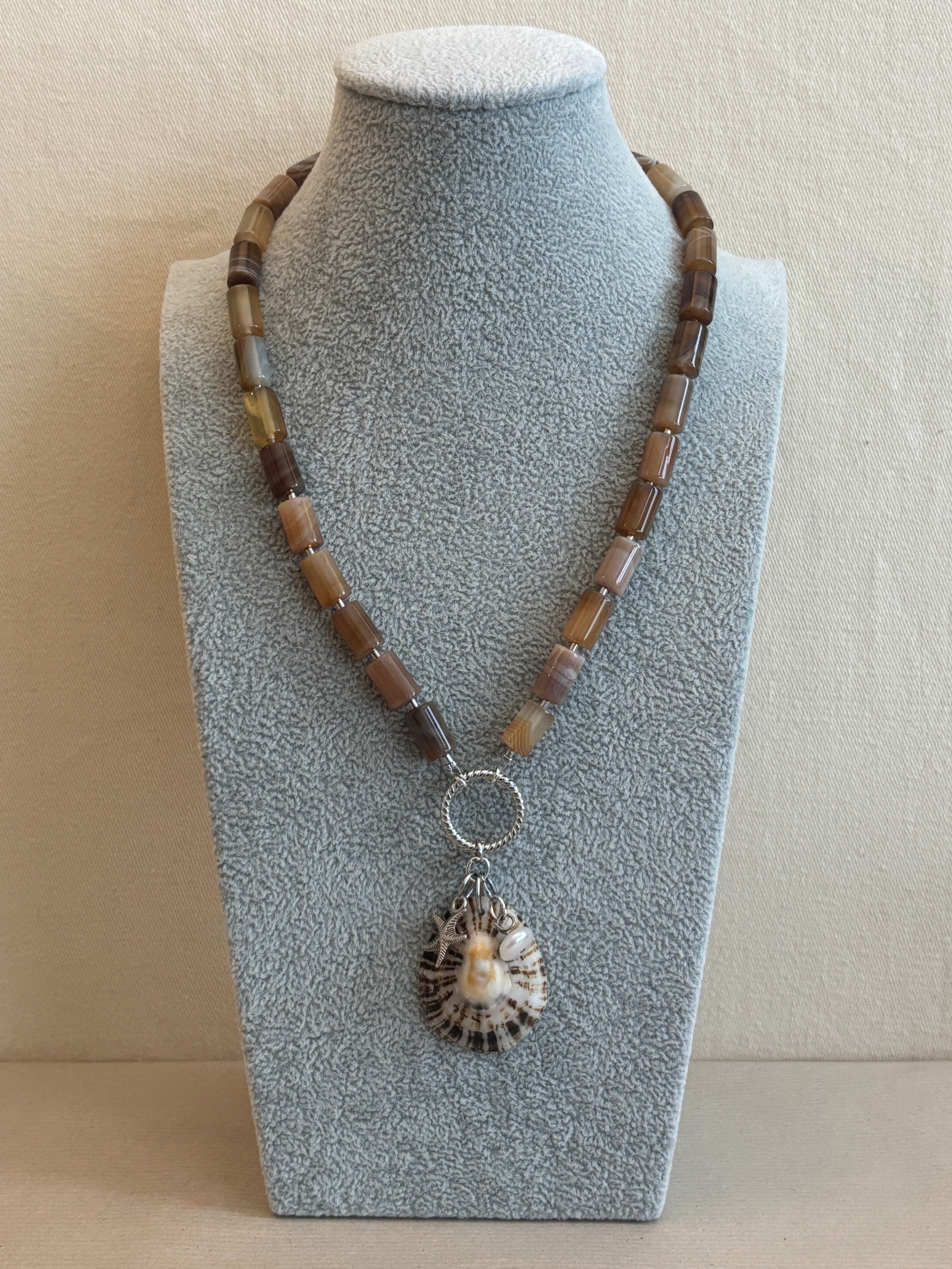 Necklace with a shell pendant on a gray stand against a beige background