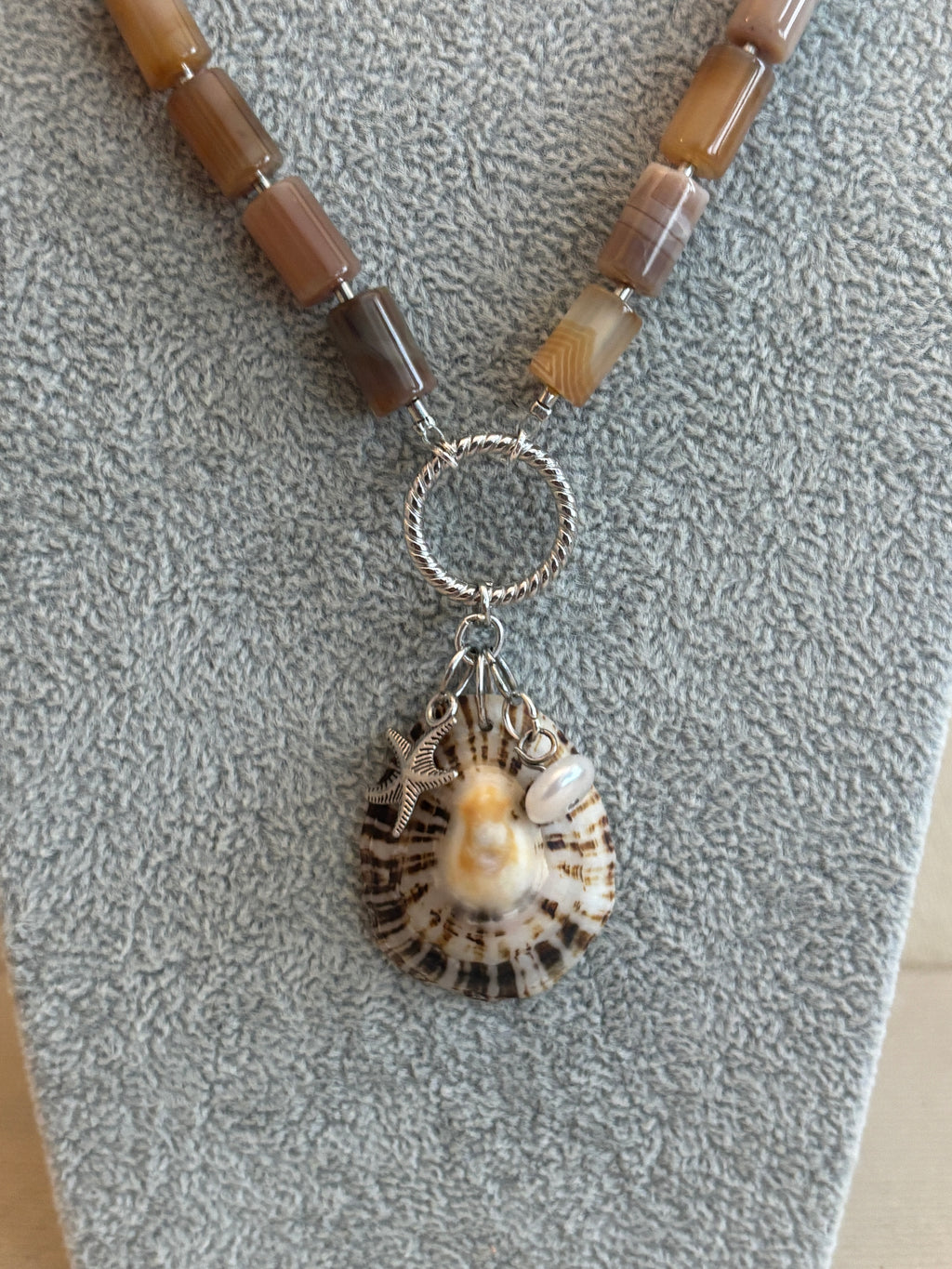 Necklace with shell and pearl charm on a textured surface