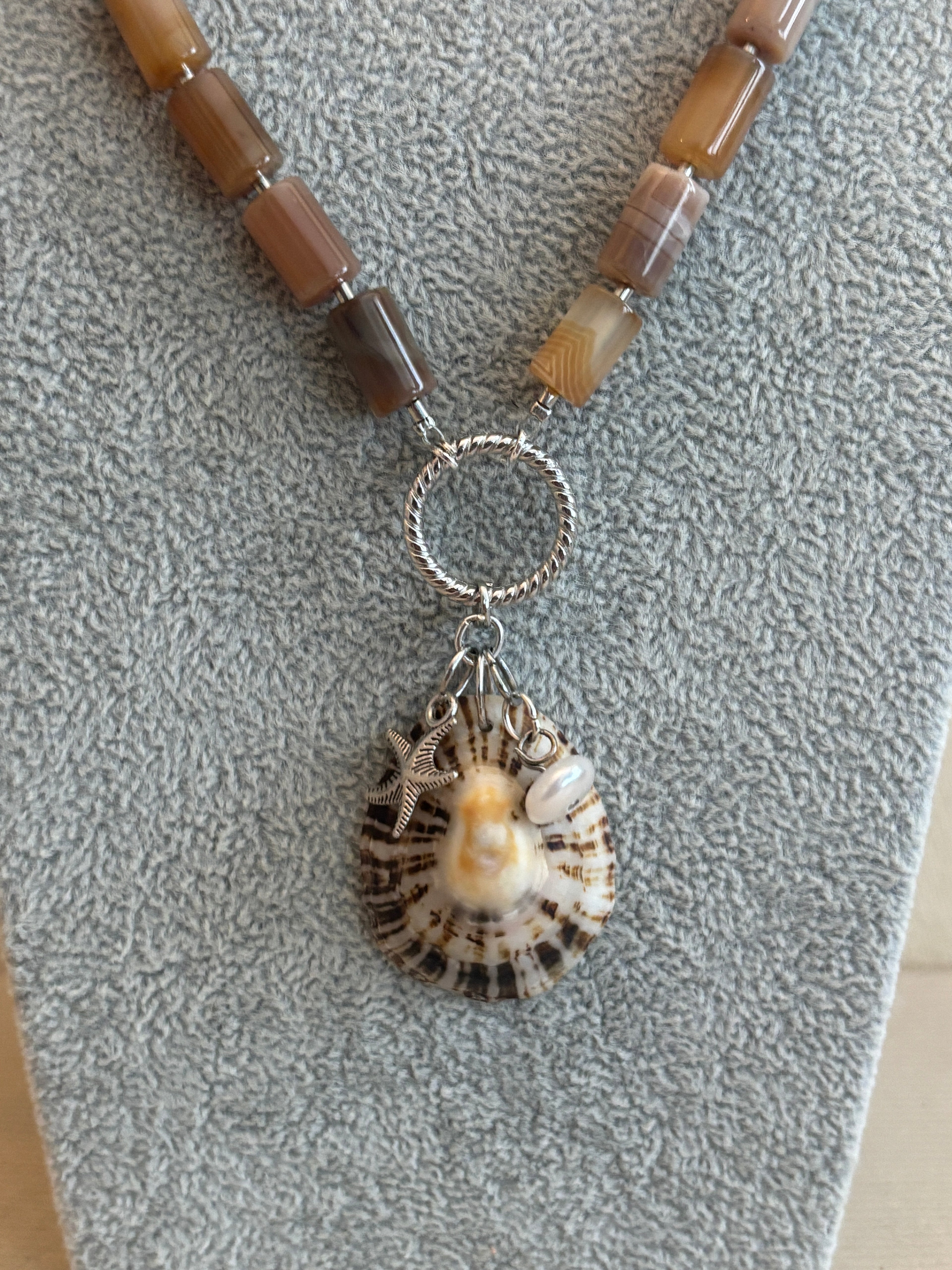 Necklace with shell and pearl charm on a textured surface