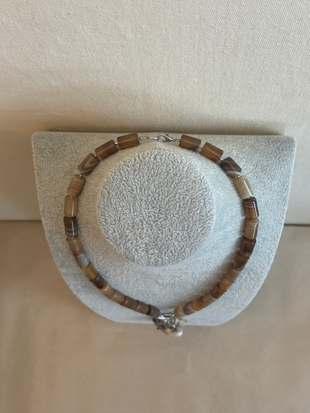 Bracelet with brown and silver beads on a textured gray stand against a beige background