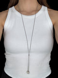 Person wearing a white tank top with a long necklace against a black background
