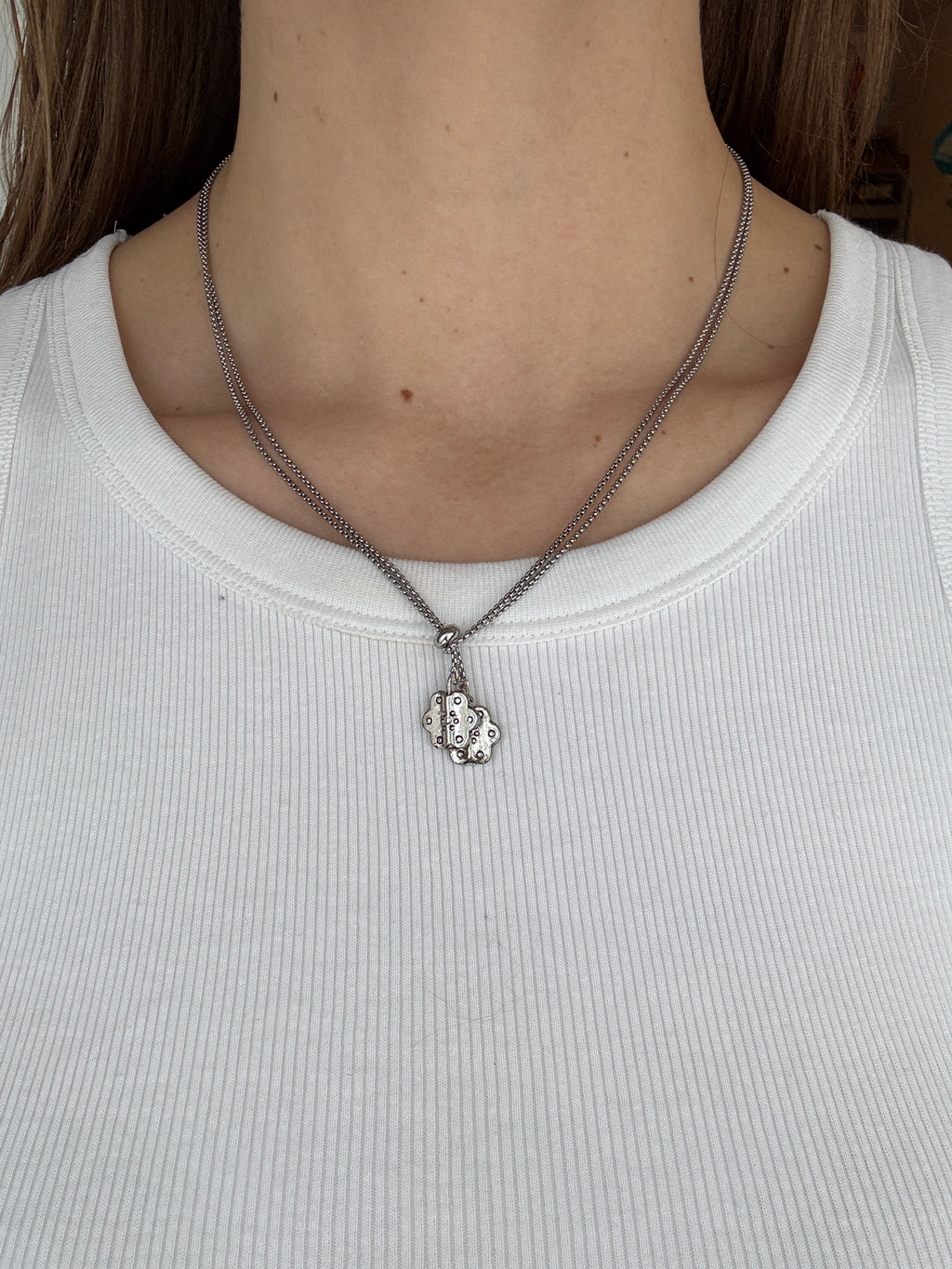 Close-up of a person wearing a thin silver chain necklace with a pendant on a plain background.