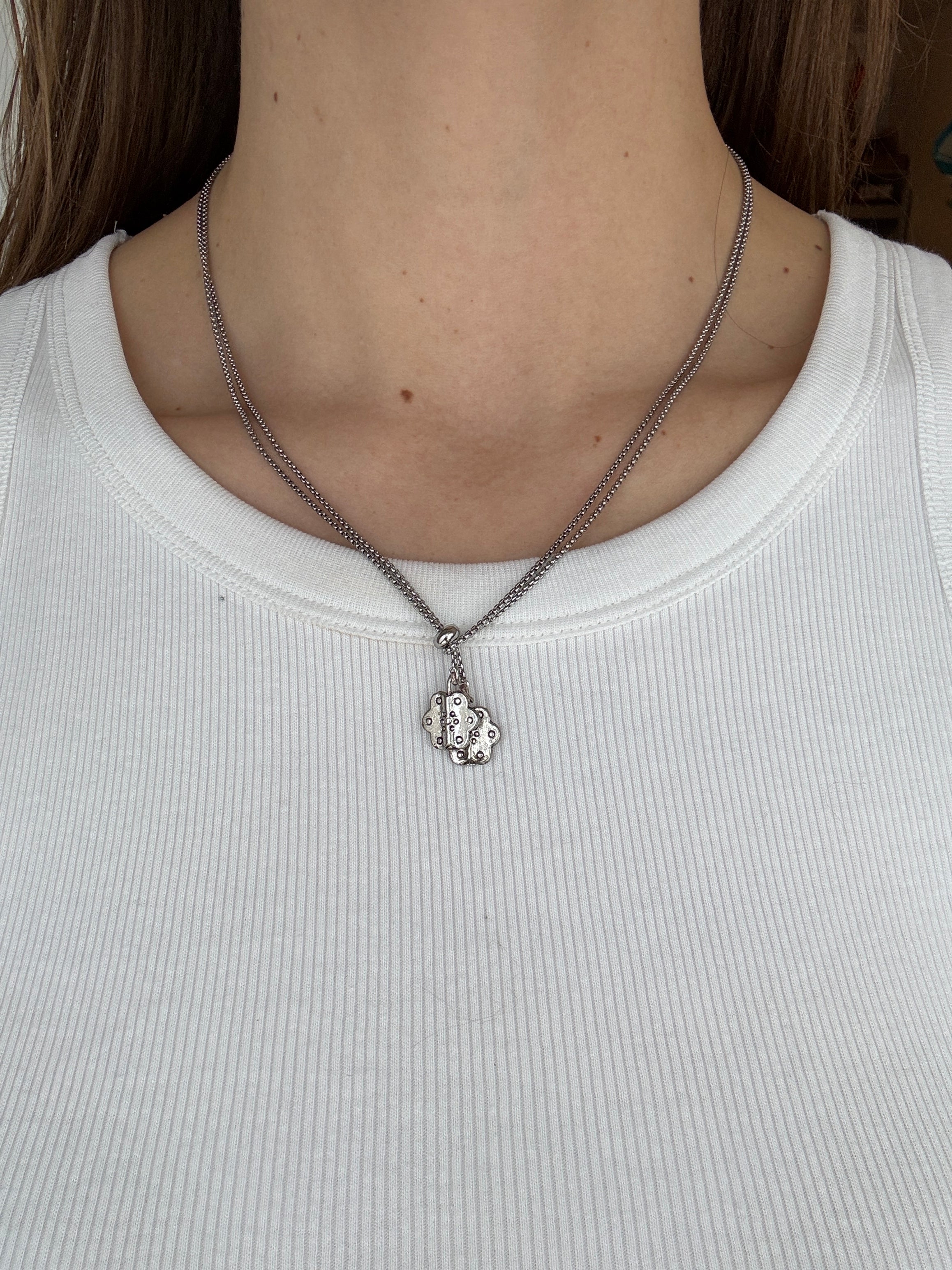 Close-up of a person wearing a thin silver chain necklace with a pendant on a plain background.