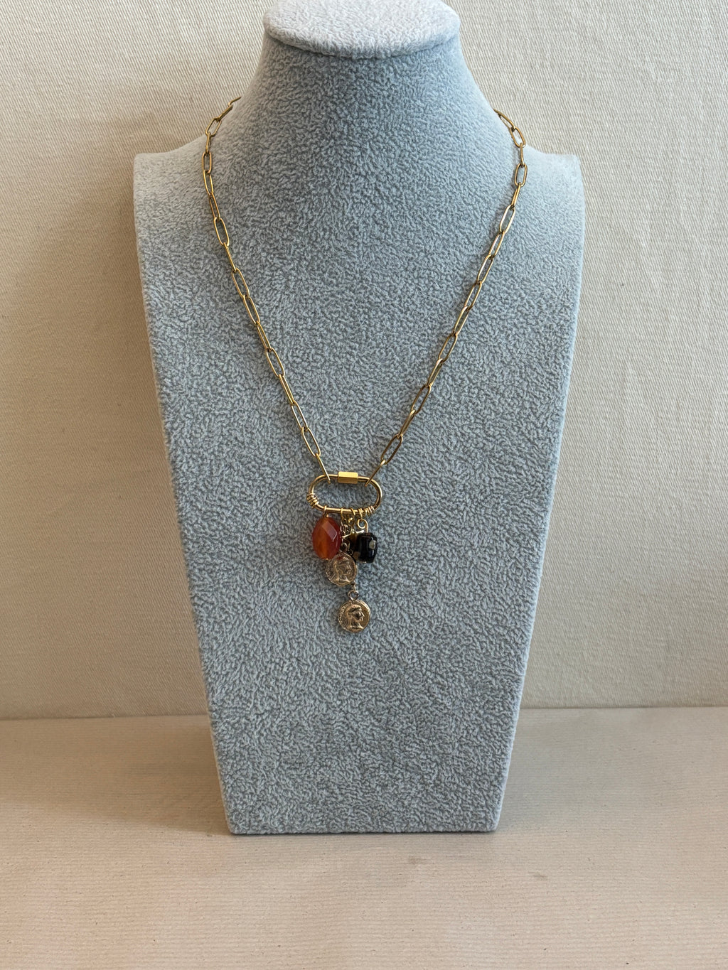 Necklace with three beads on a gray velvet stand against a beige background