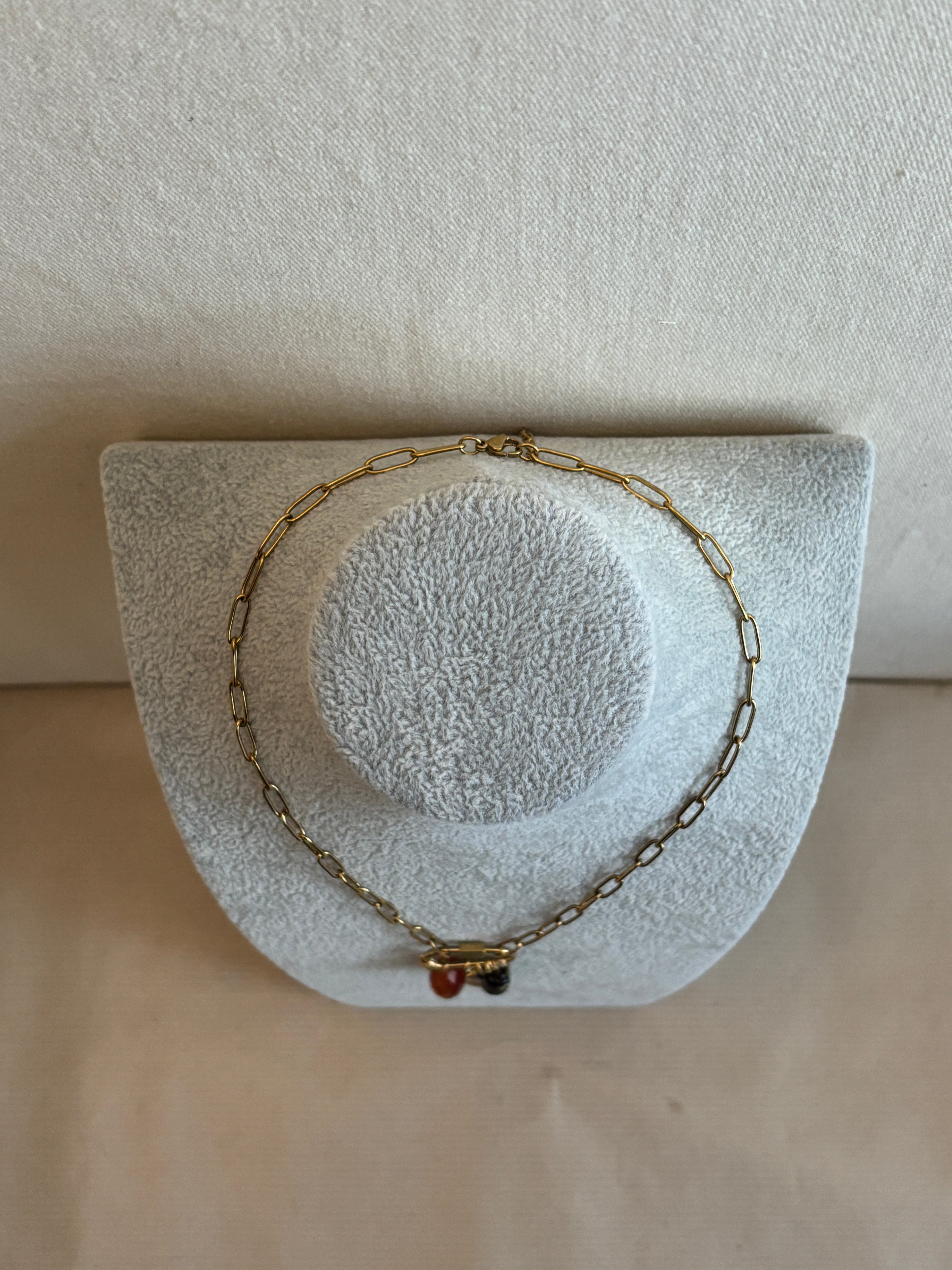Gold necklace on a textured white stand against a beige background