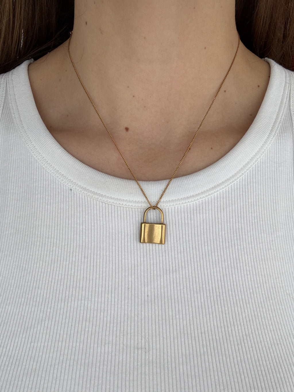 Close-up of a person wearing a white tank top with a gold necklace.
