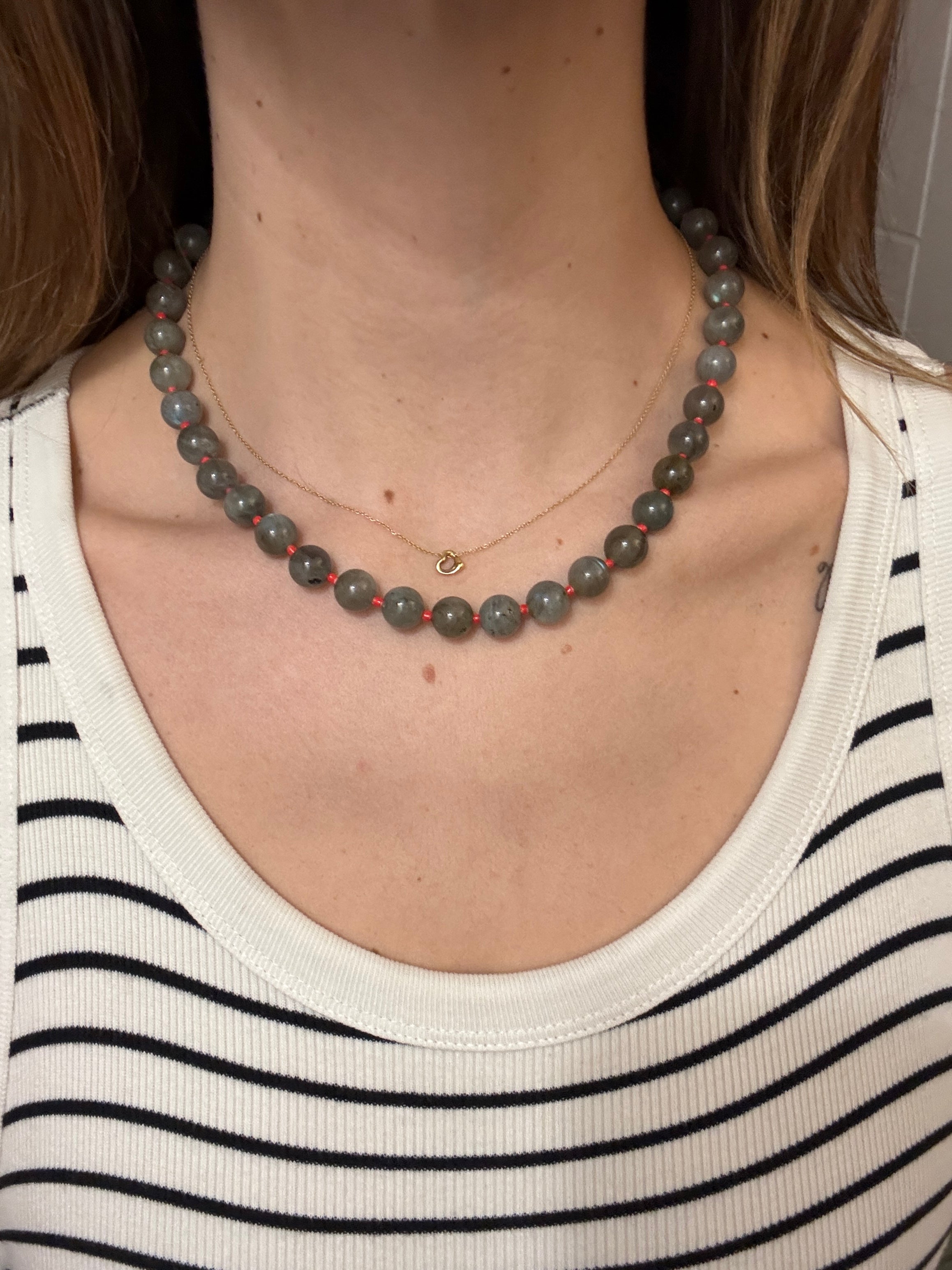 Person wearing a gray beaded necklace with a white tank top featuring black stripes.