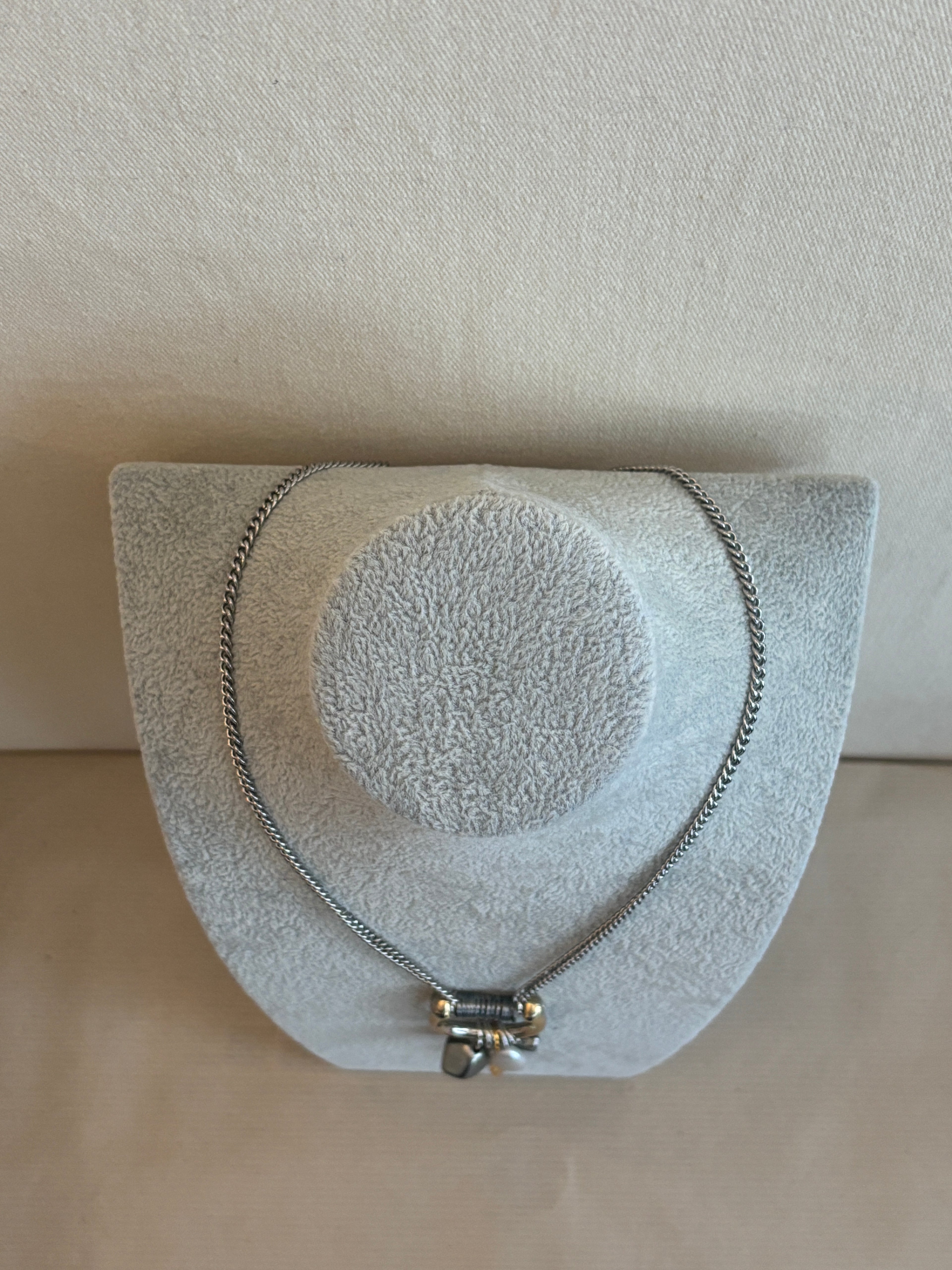 Silver necklace on a gray jewelry display block against a beige background