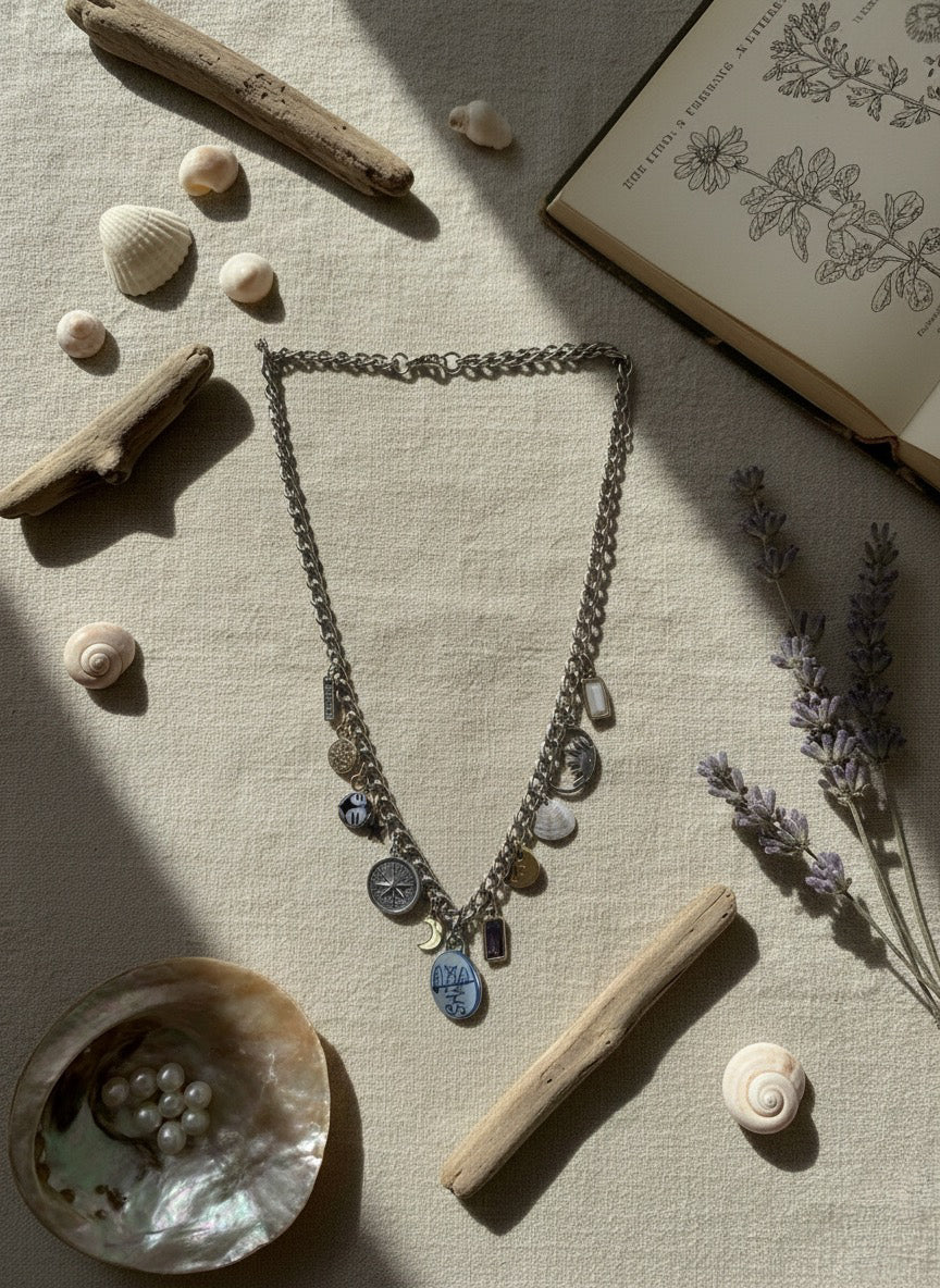 Necklace with charms on a textured surface with shells, driftwood, and a book