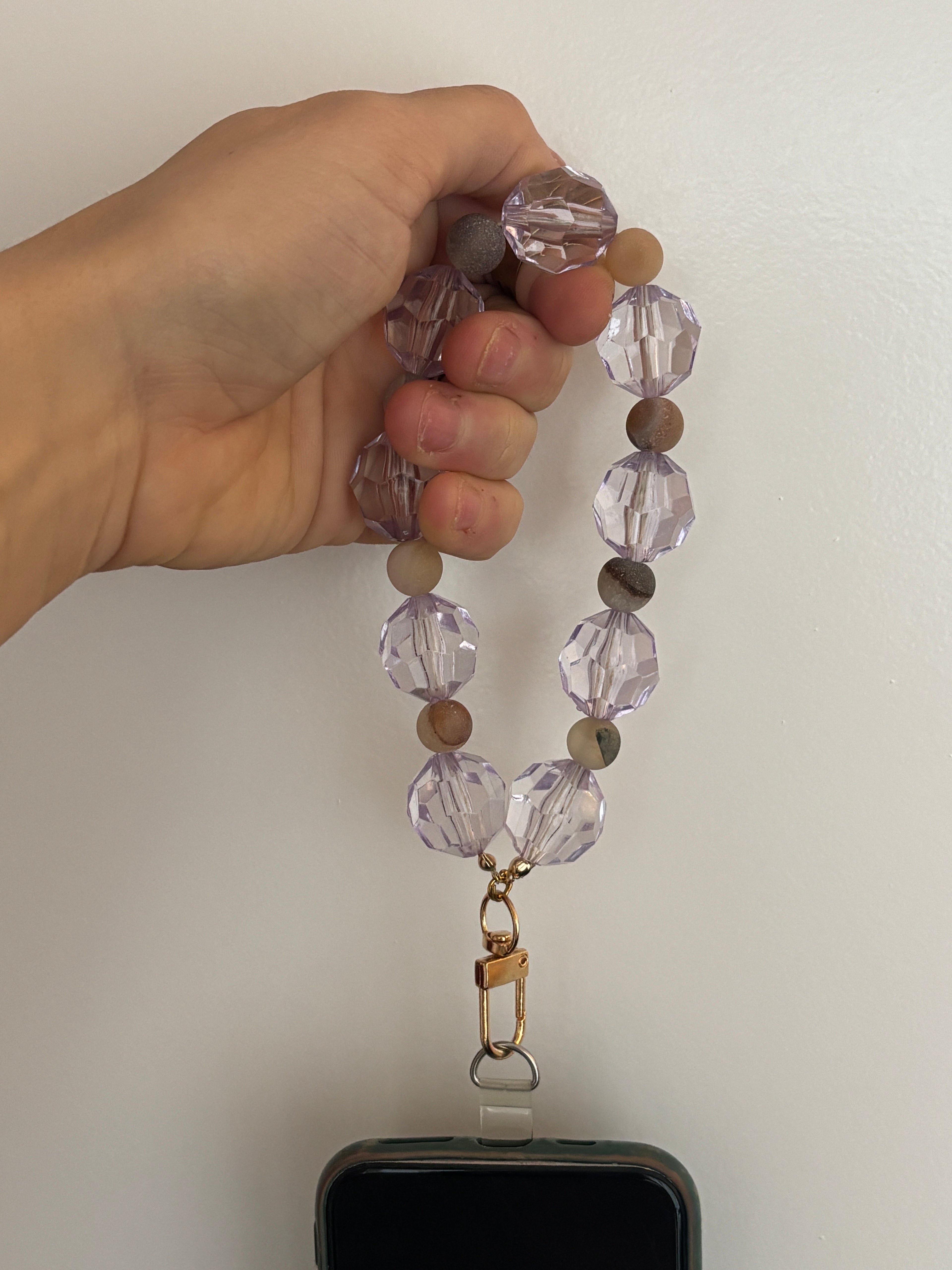 Hand holding a beaded phone lanyard with a smartphone on a white background