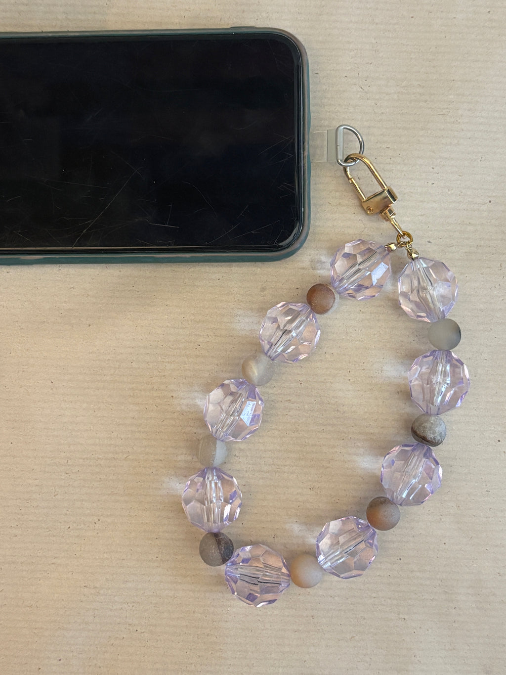 Beaded phone strap with clear and brown beads on a beige surface