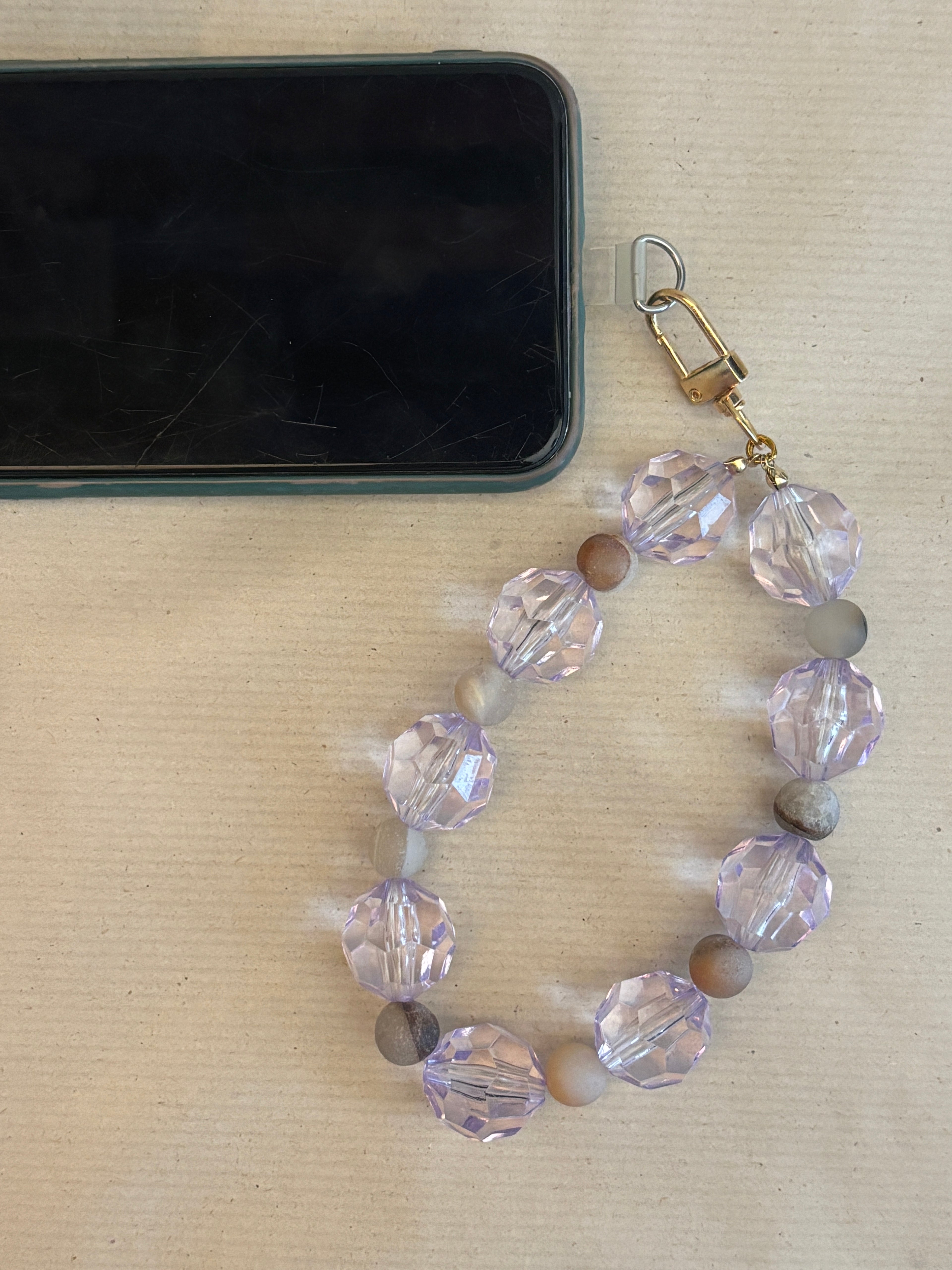 Beaded phone strap with clear and brown beads on a beige surface