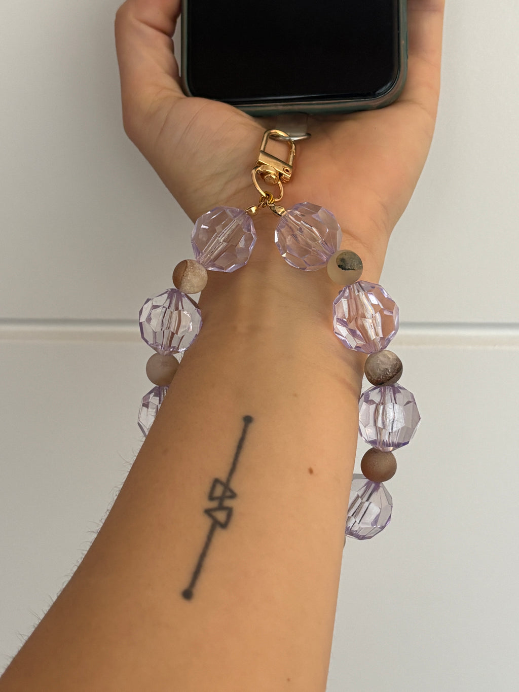 Hand wearing a bracelet with clear lilac and white beads, holding a phone against a white background