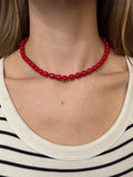 Close-up of a person wearing a red beaded necklace with a neutral background