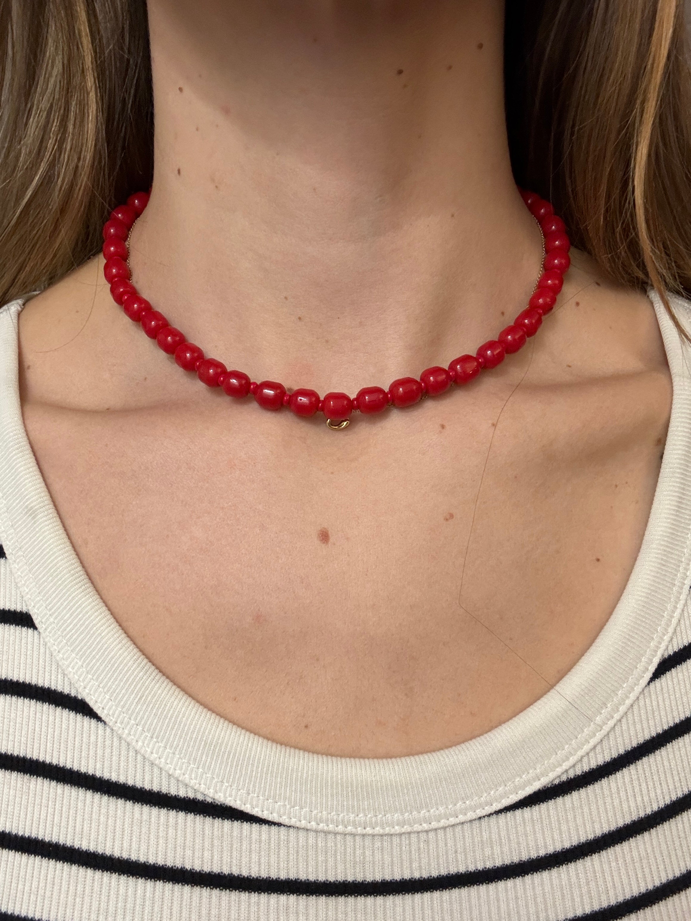 Close-up of a person wearing a red beaded necklace with a neutral background
