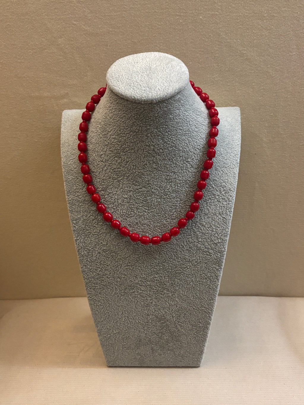 Red beaded necklace on a gray stand against a beige background