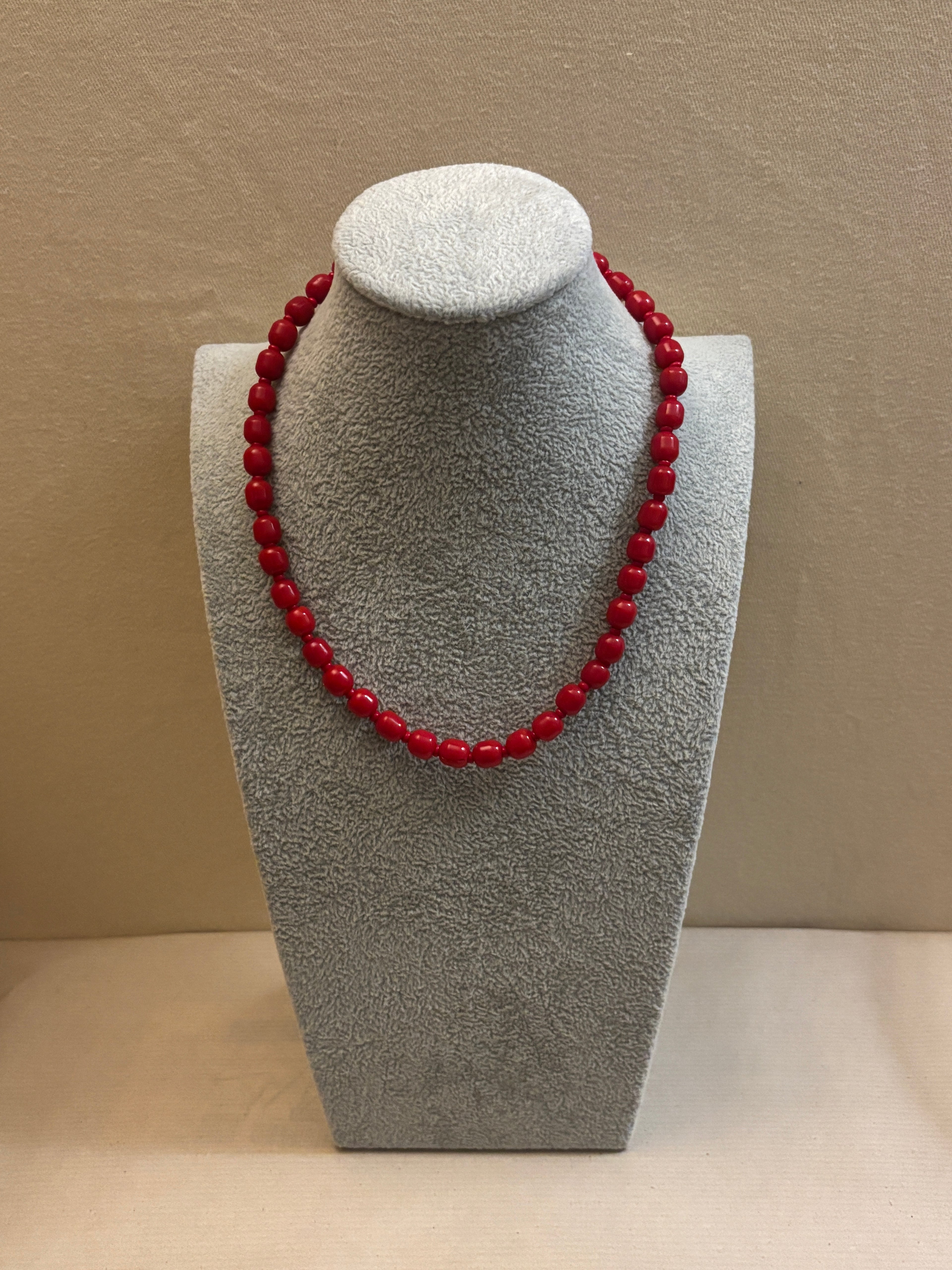 Red beaded necklace on a gray stand against a beige background