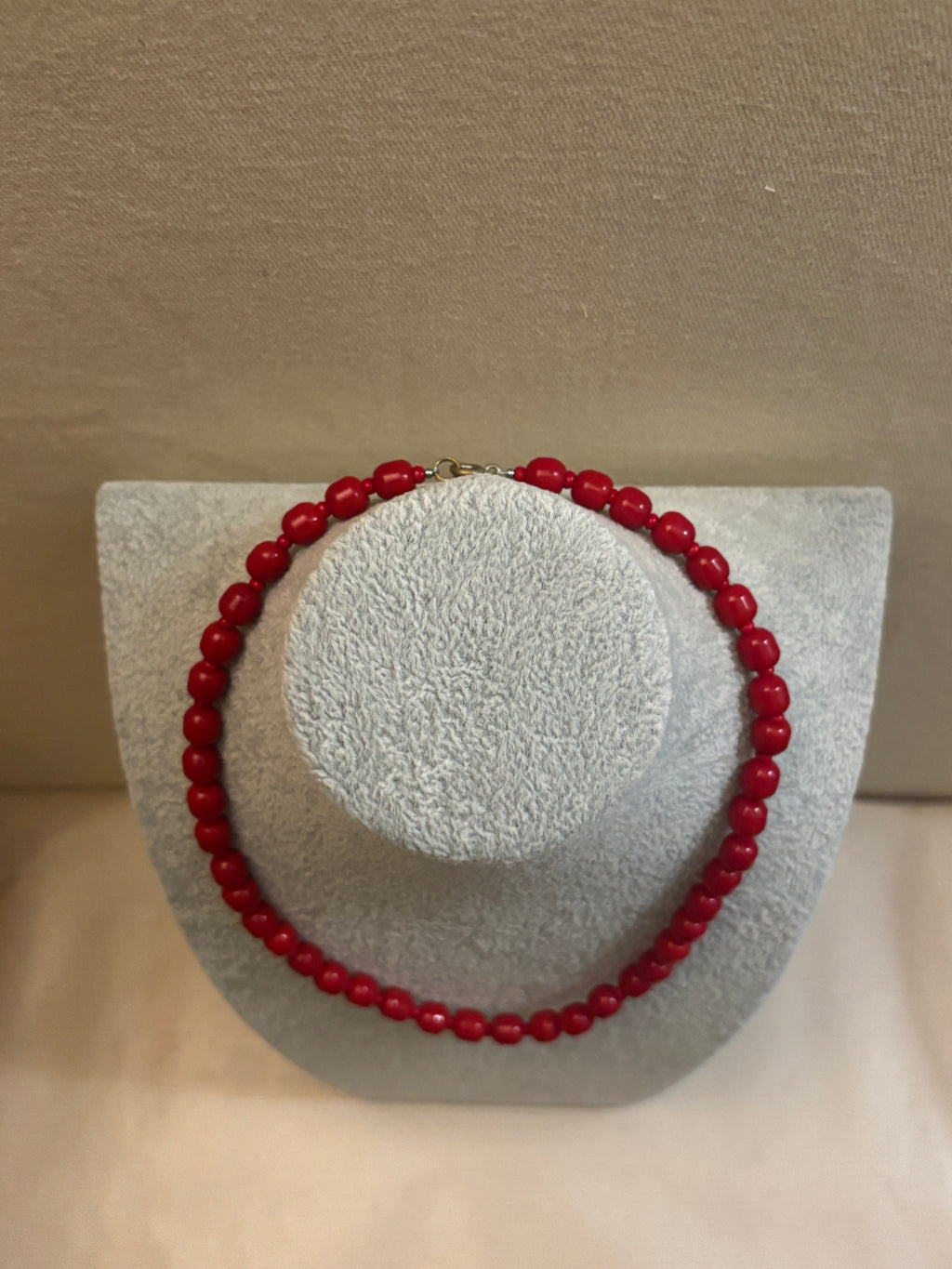 Red beaded bracelet on a textured gray stand against a beige background