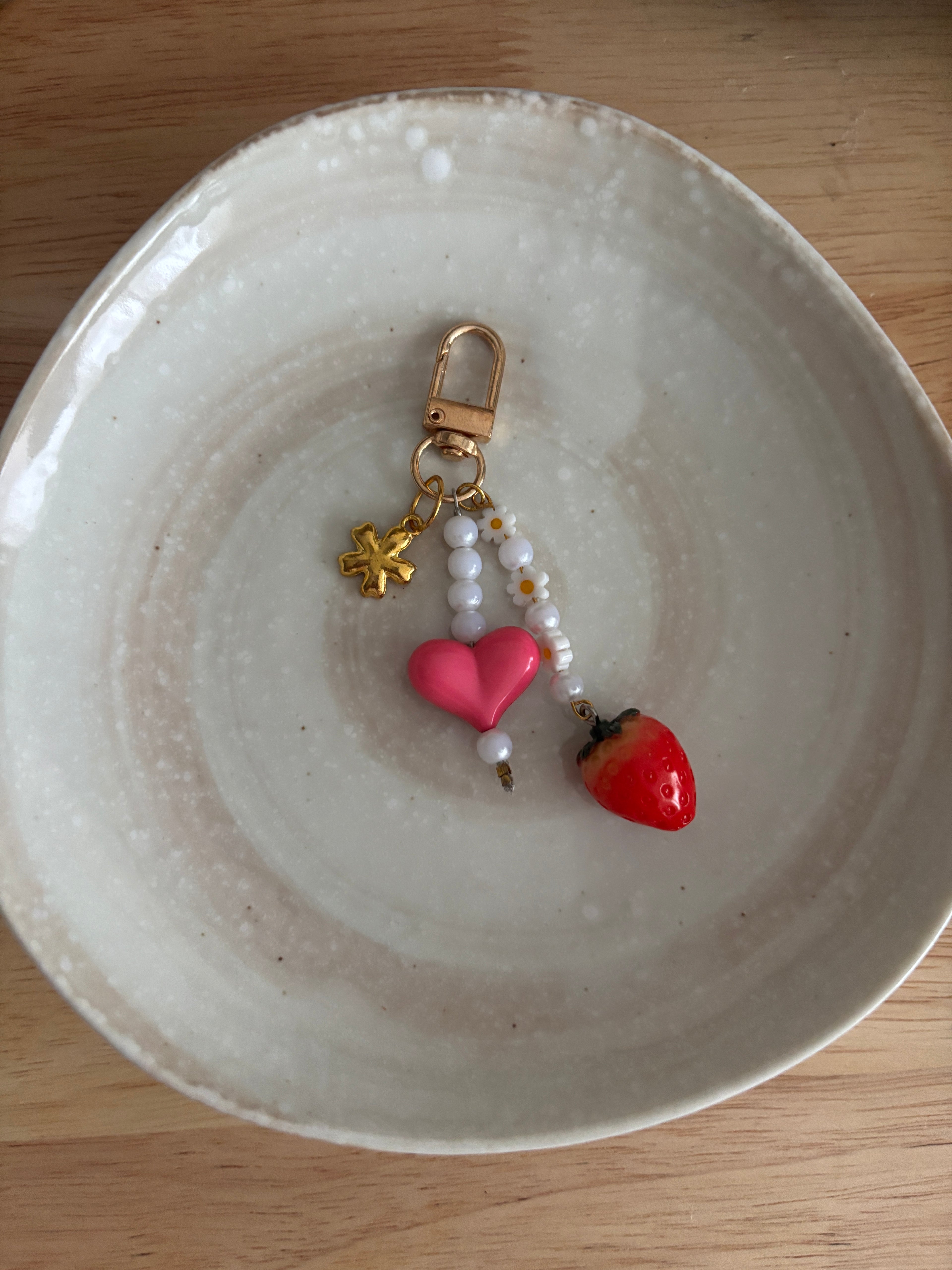 Decorative keychain with heart and strawberry charms on a ceramic plate.