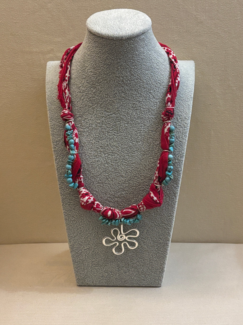 Decorative necklace with floral design on a gray stand against a beige background