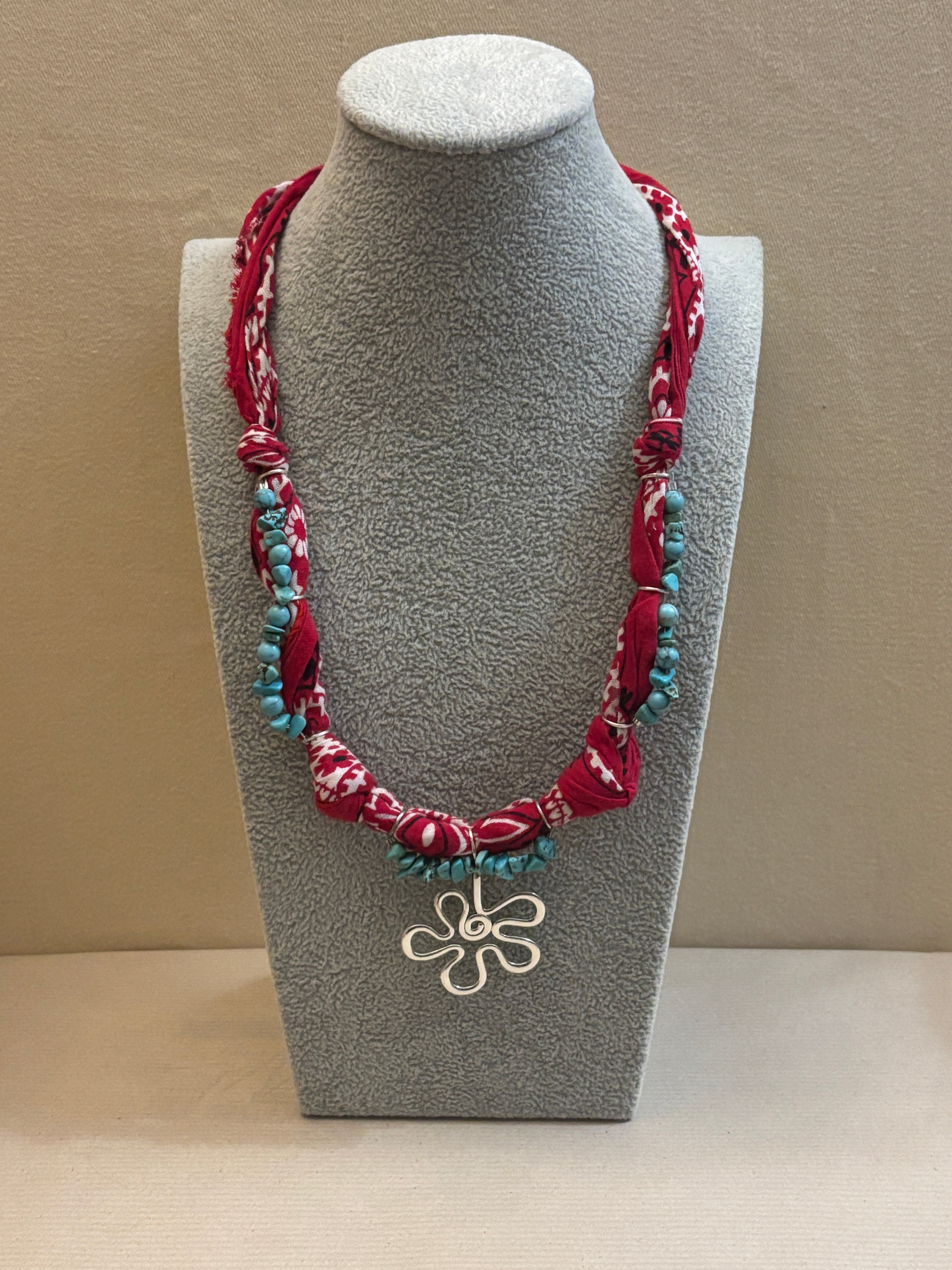Decorative necklace with floral design on a gray stand against a beige background