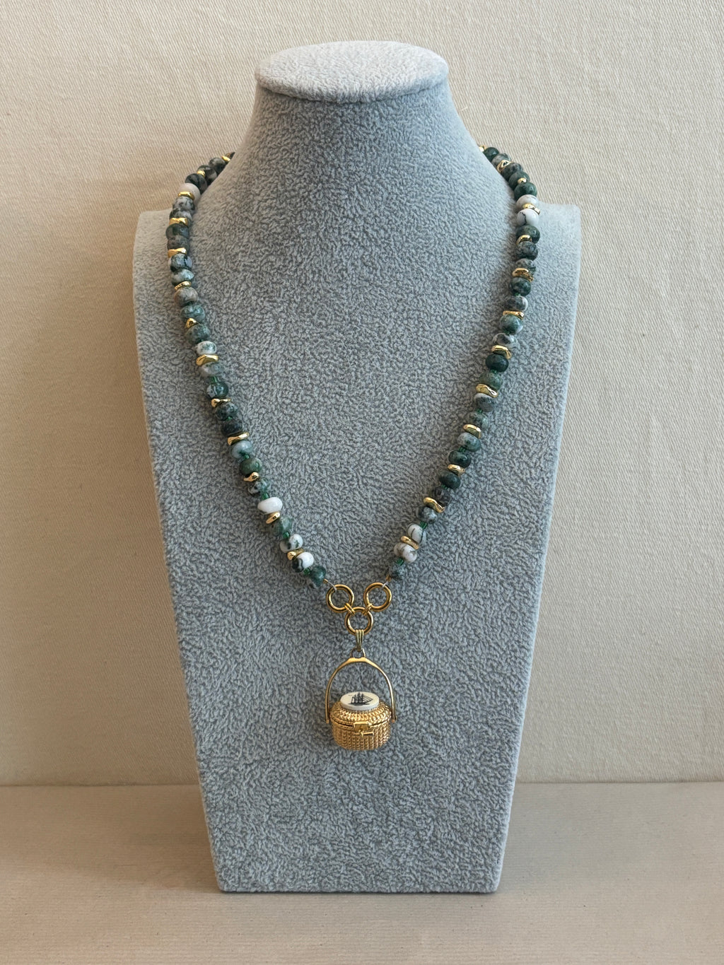 Necklace with green beads and gold clasp on a gray jewelry display