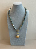 Necklace with green beads and gold clasp on a gray jewelry display
