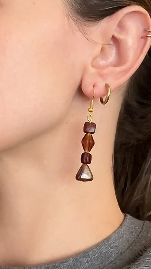 Close-up of an ear wearing a gold earring with brown beads.