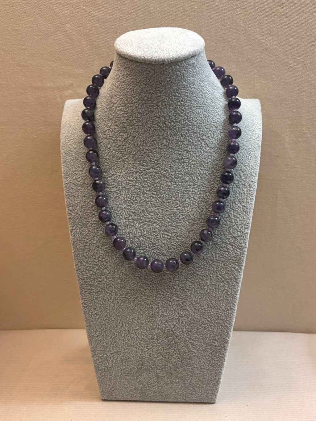 Amethyst necklace on a gray bust against a beige background