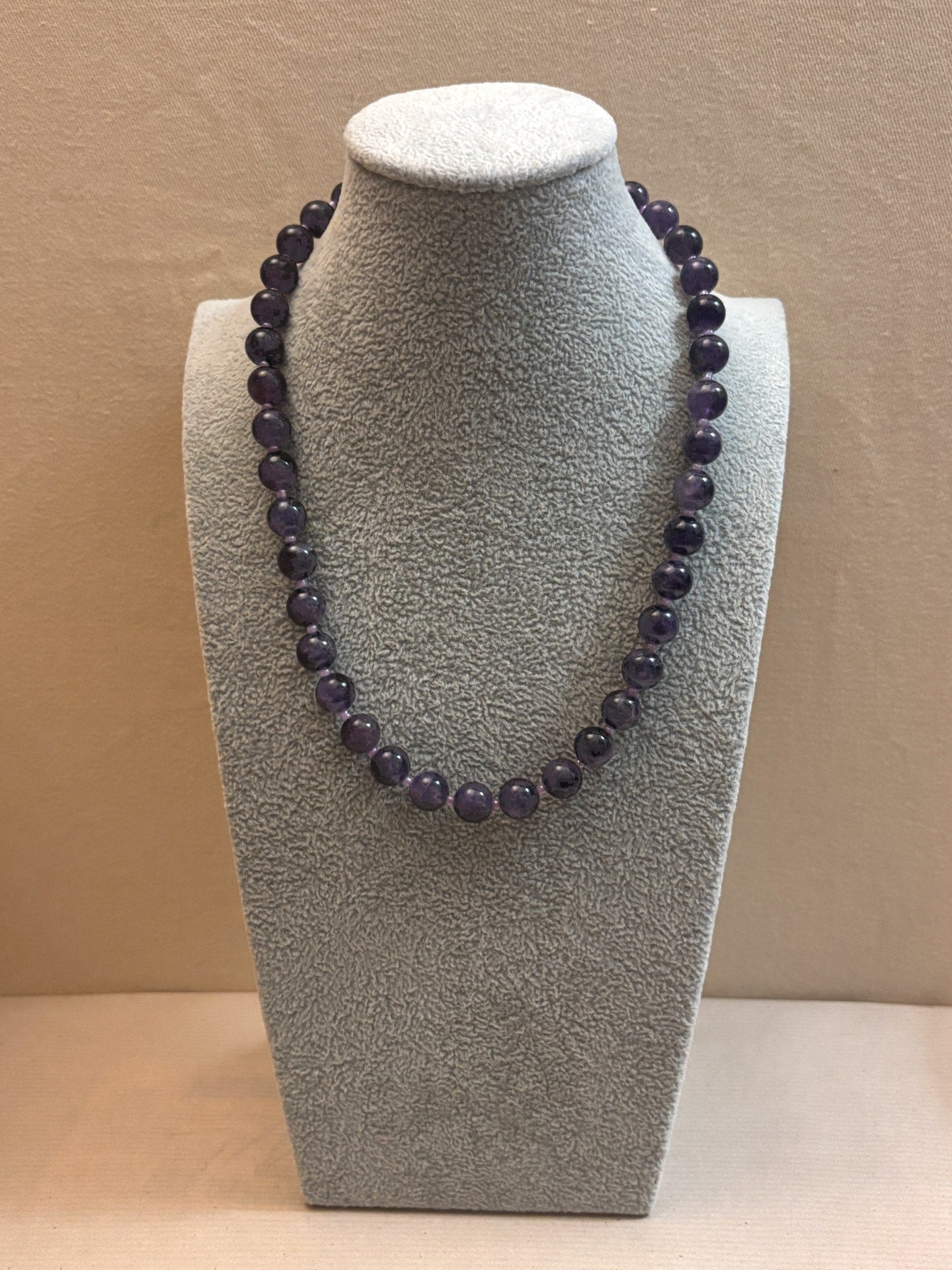 Amethyst necklace on a gray bust against a beige background