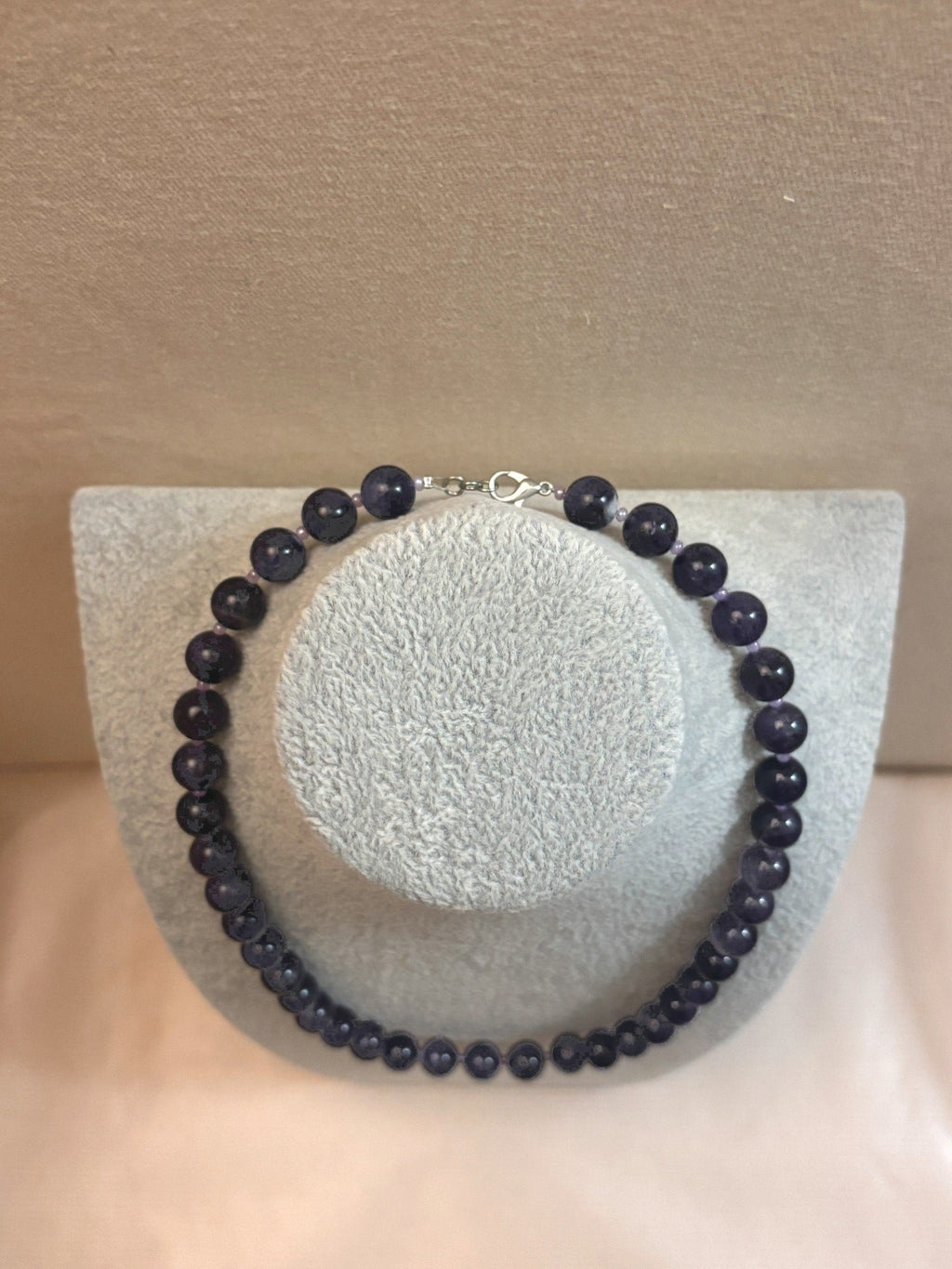 Necklace with dark beads on a mannequin bust against a beige background