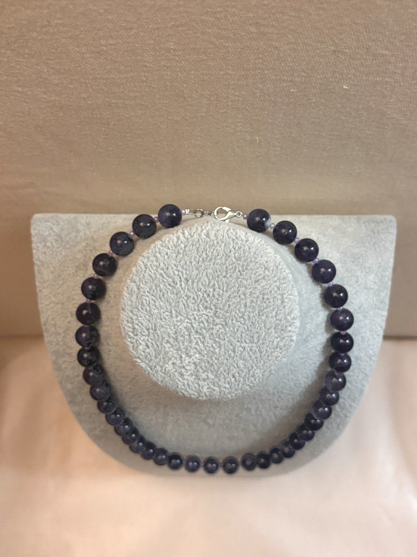 Necklace with dark beads on a mannequin bust against a beige background