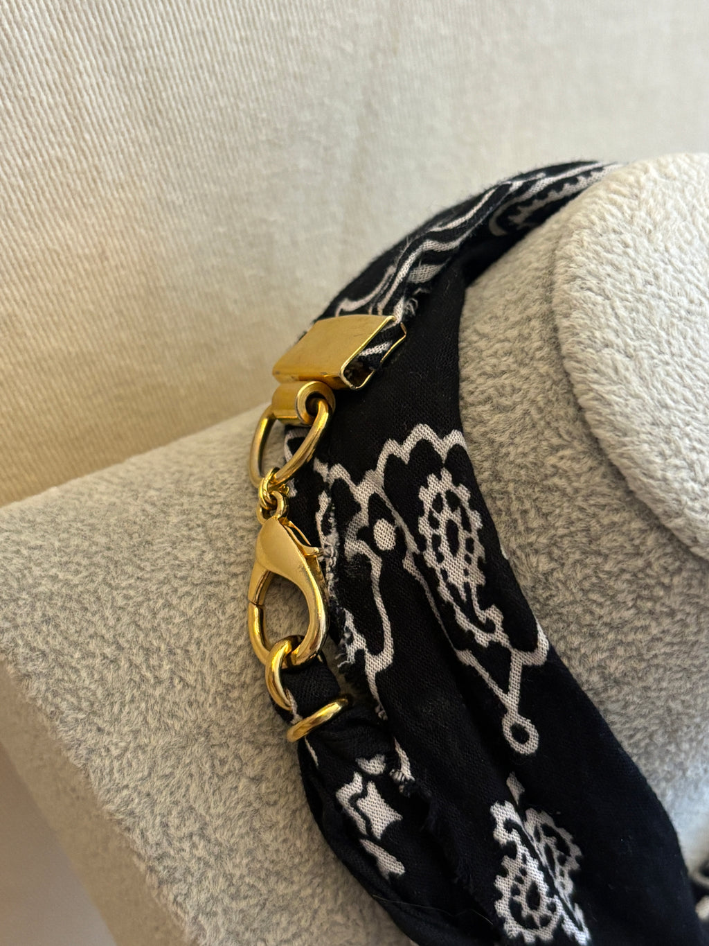 Black bandana with white patterns and gold buckle on a mannequin head.
