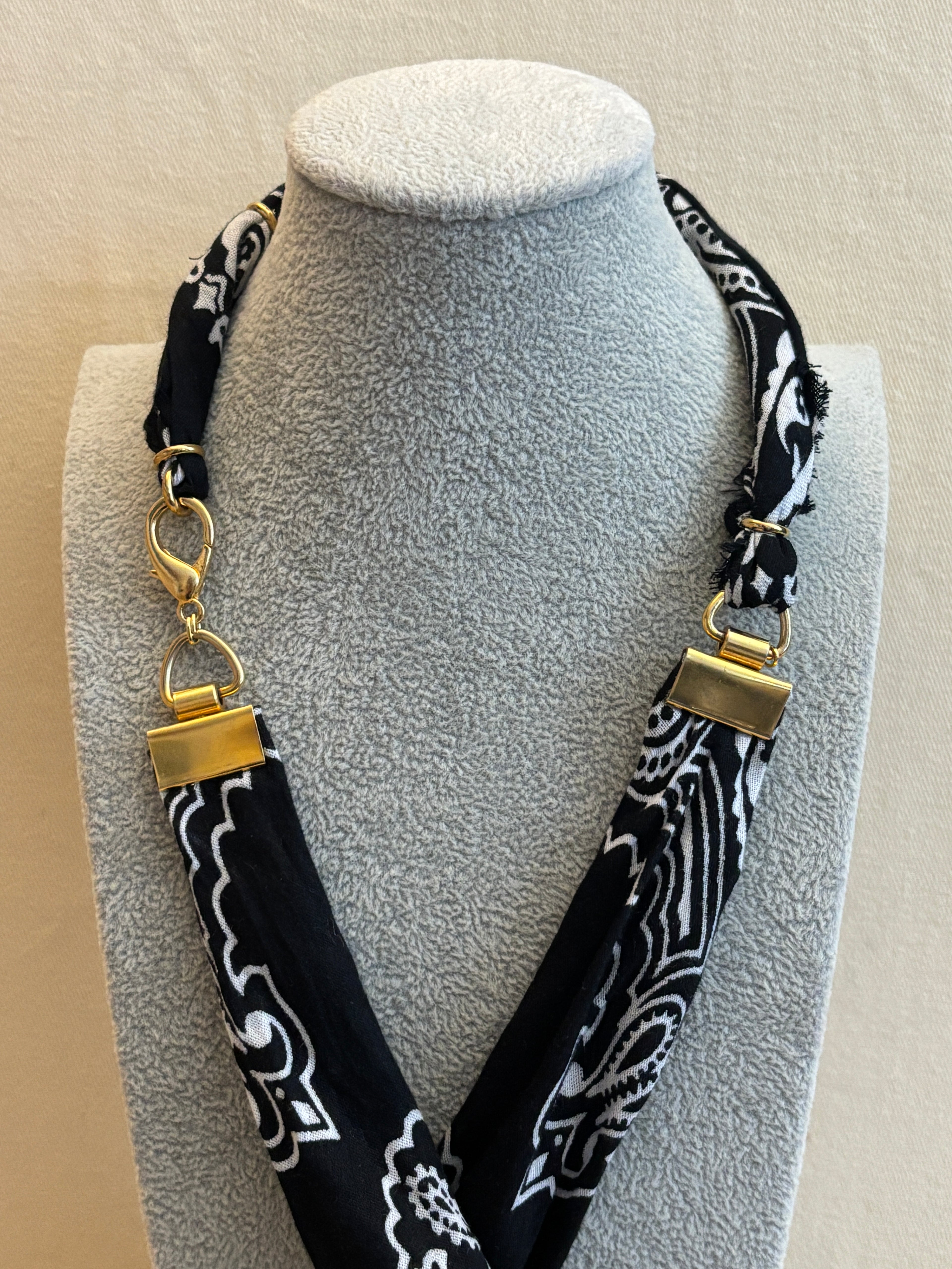 Black and white patterned headband with gold accents on a gray stand