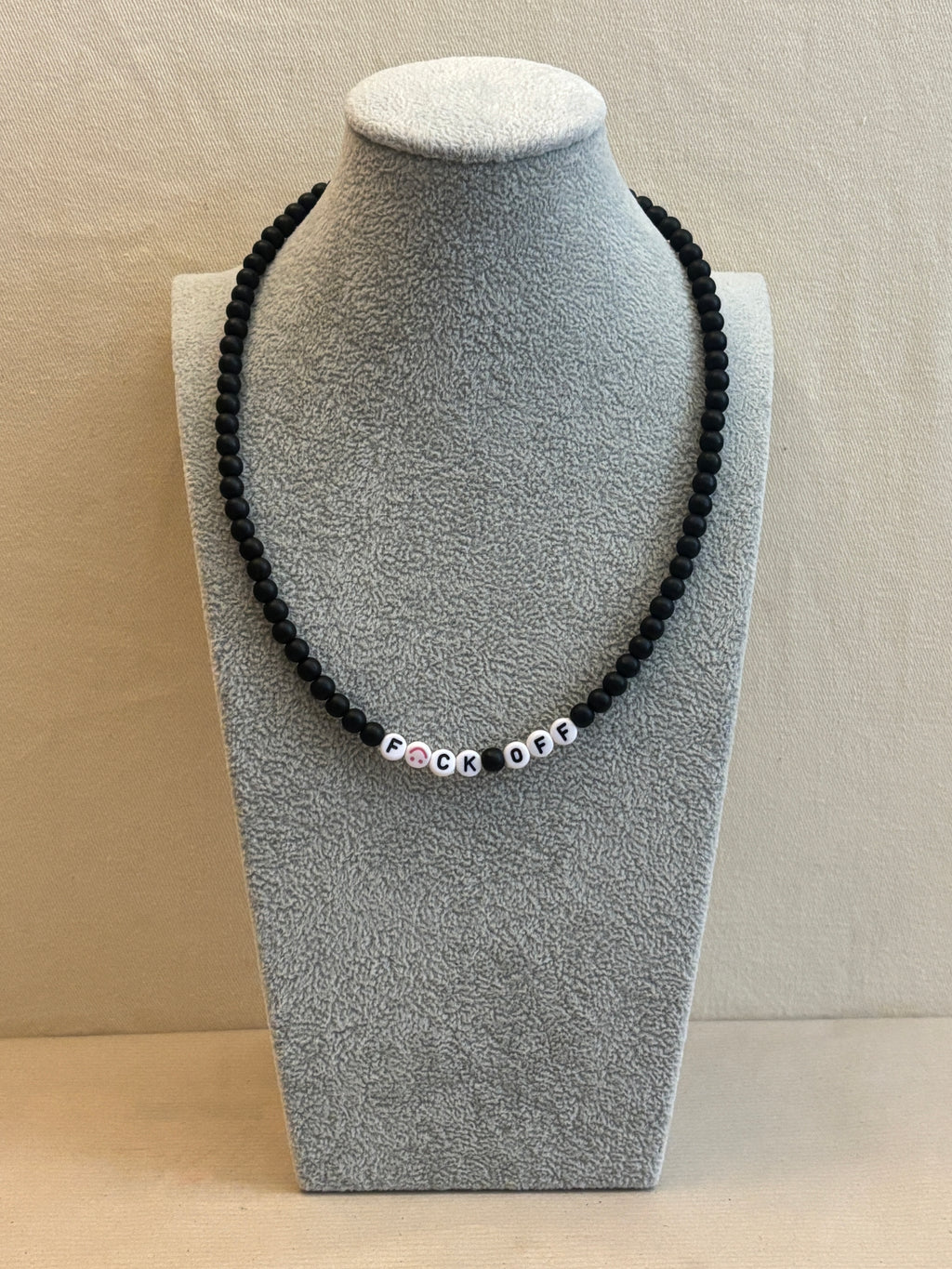 Black beaded necklace on a gray jewelry display block against a beige background