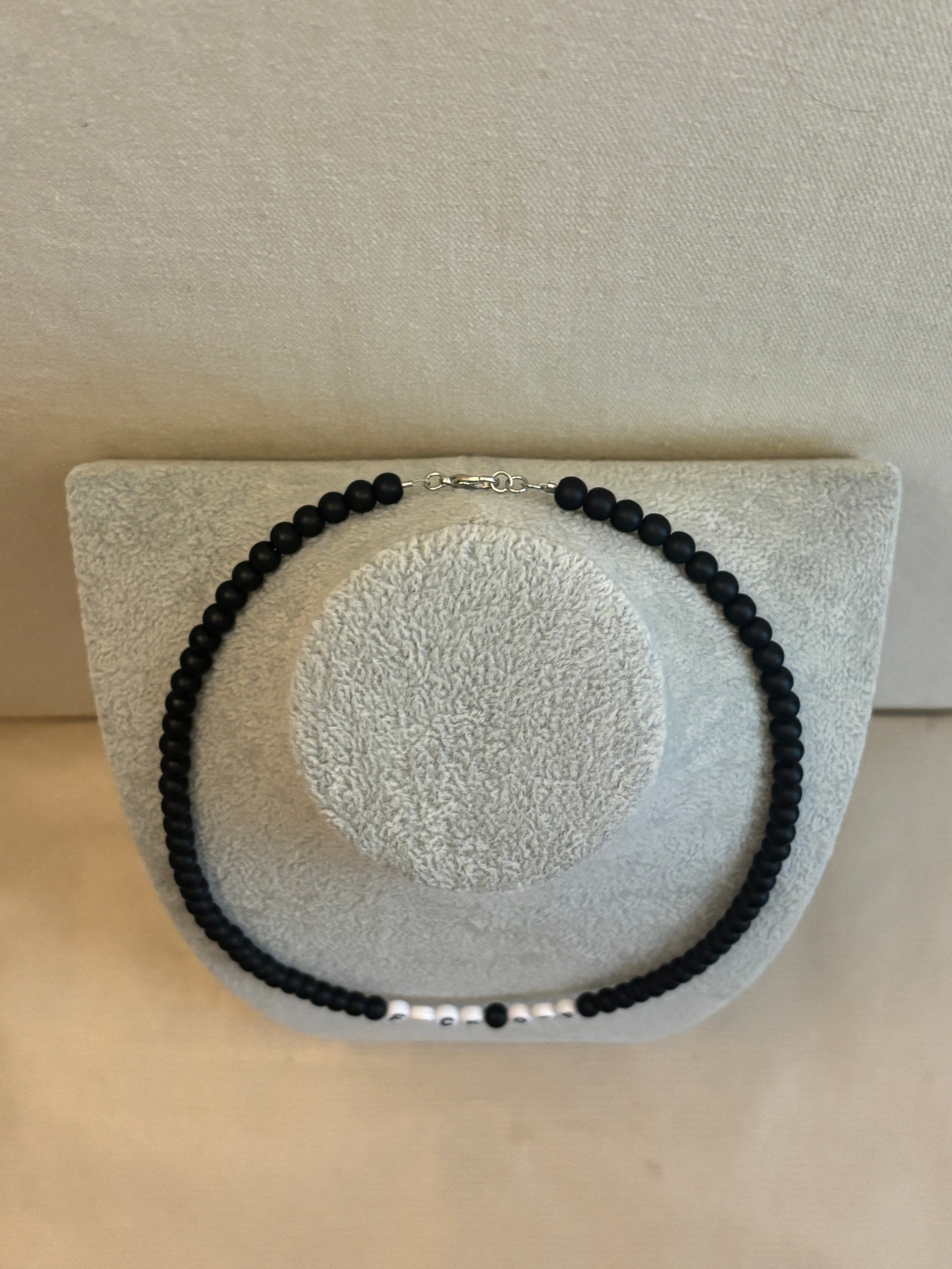 Black beaded necklace on a textured stone stand against a beige background