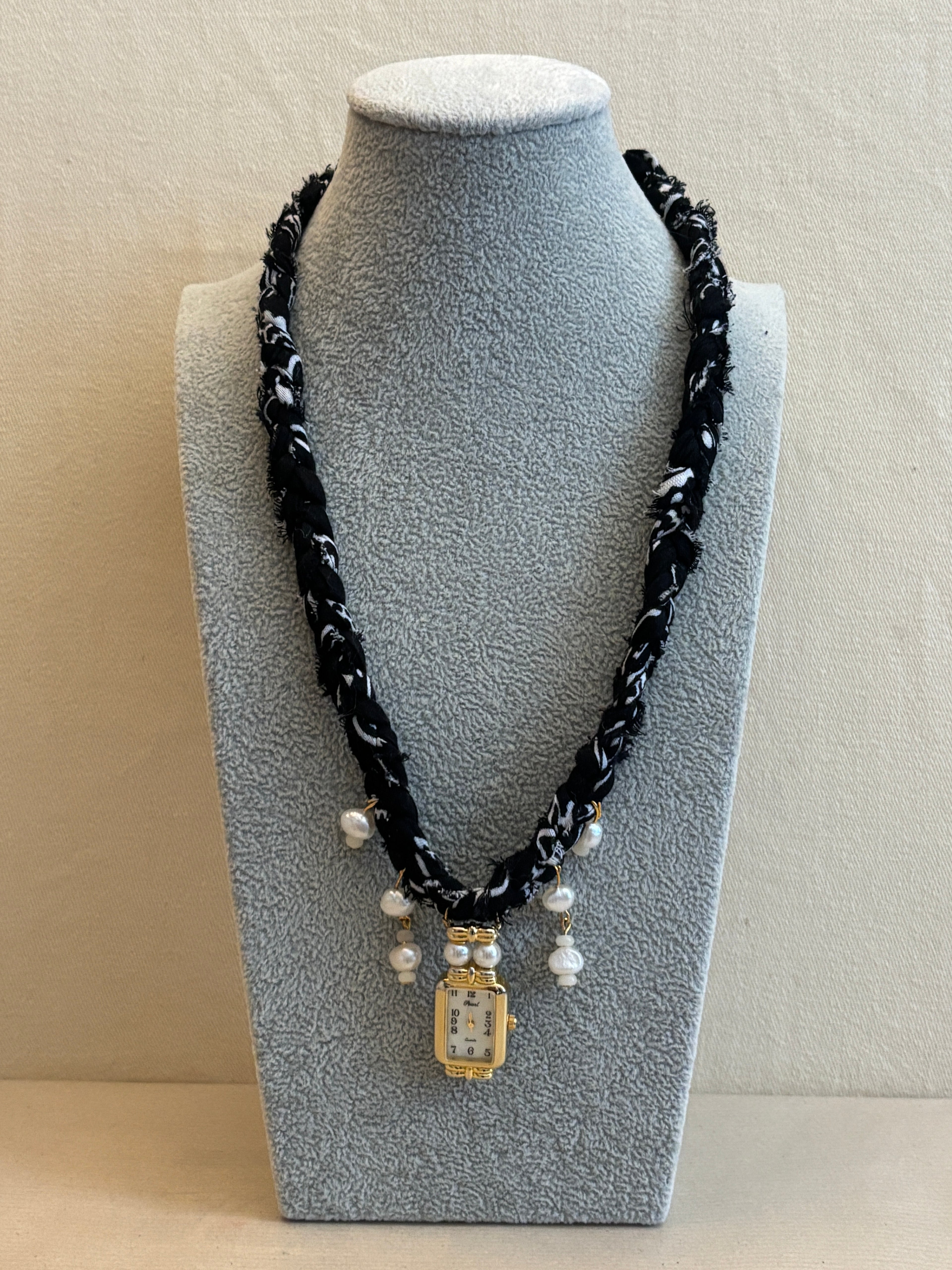 Necklace with black braided bandana and white pearls on a gray stand against a beige background