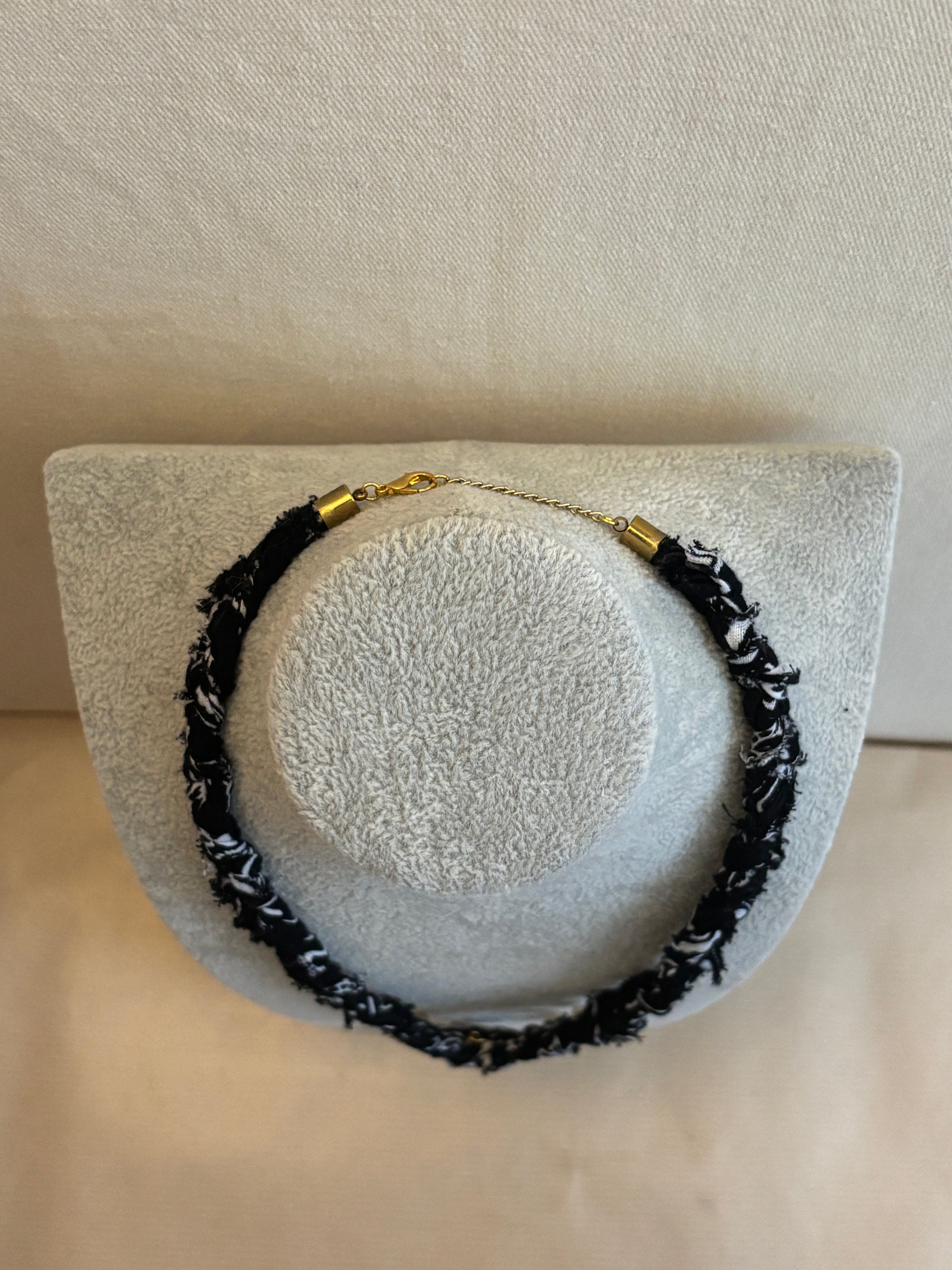 Necklace with black and gold elements on a white stand against a beige background